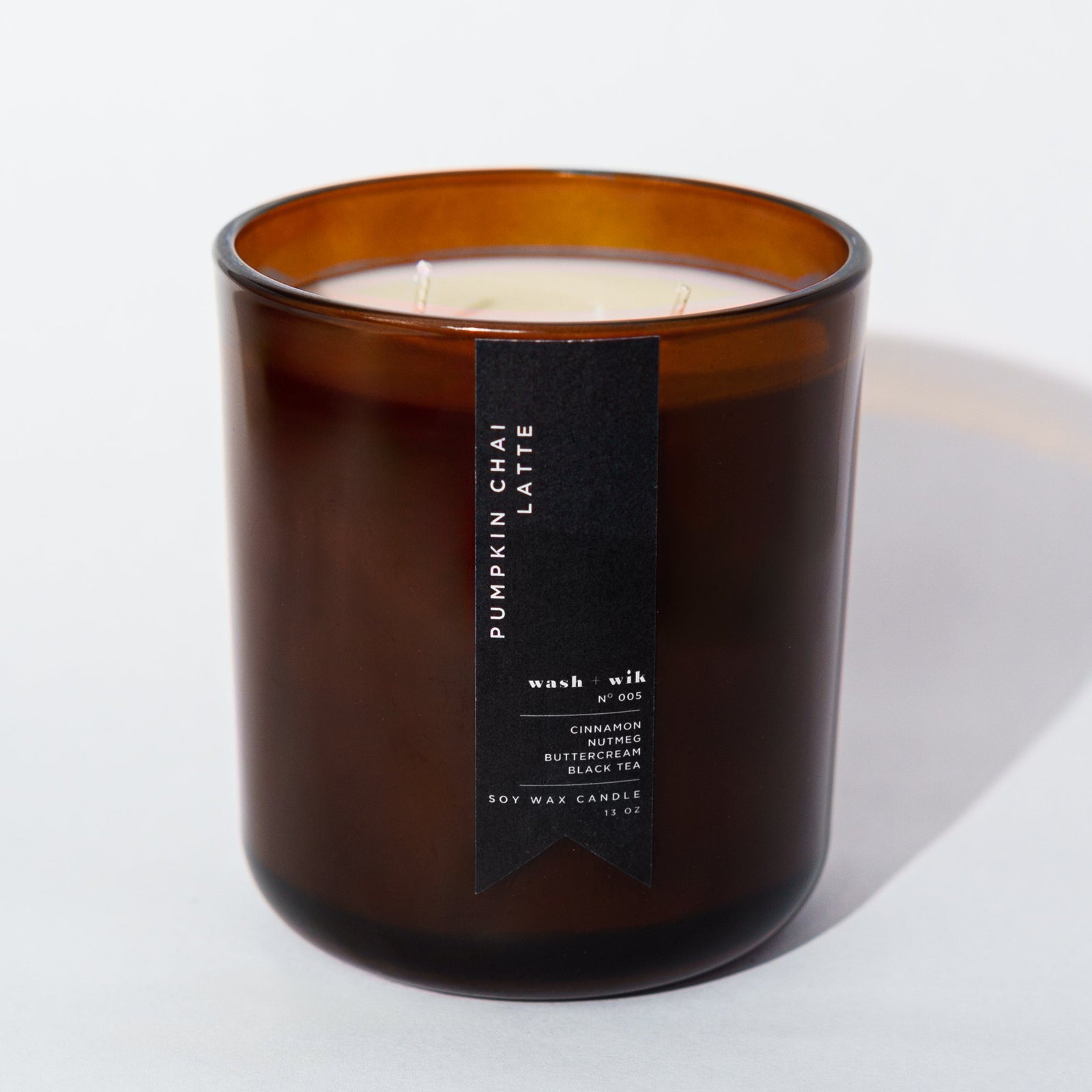 An amber glass jar candle with a black vertical label photographed on a clean white background with a soft shadow.