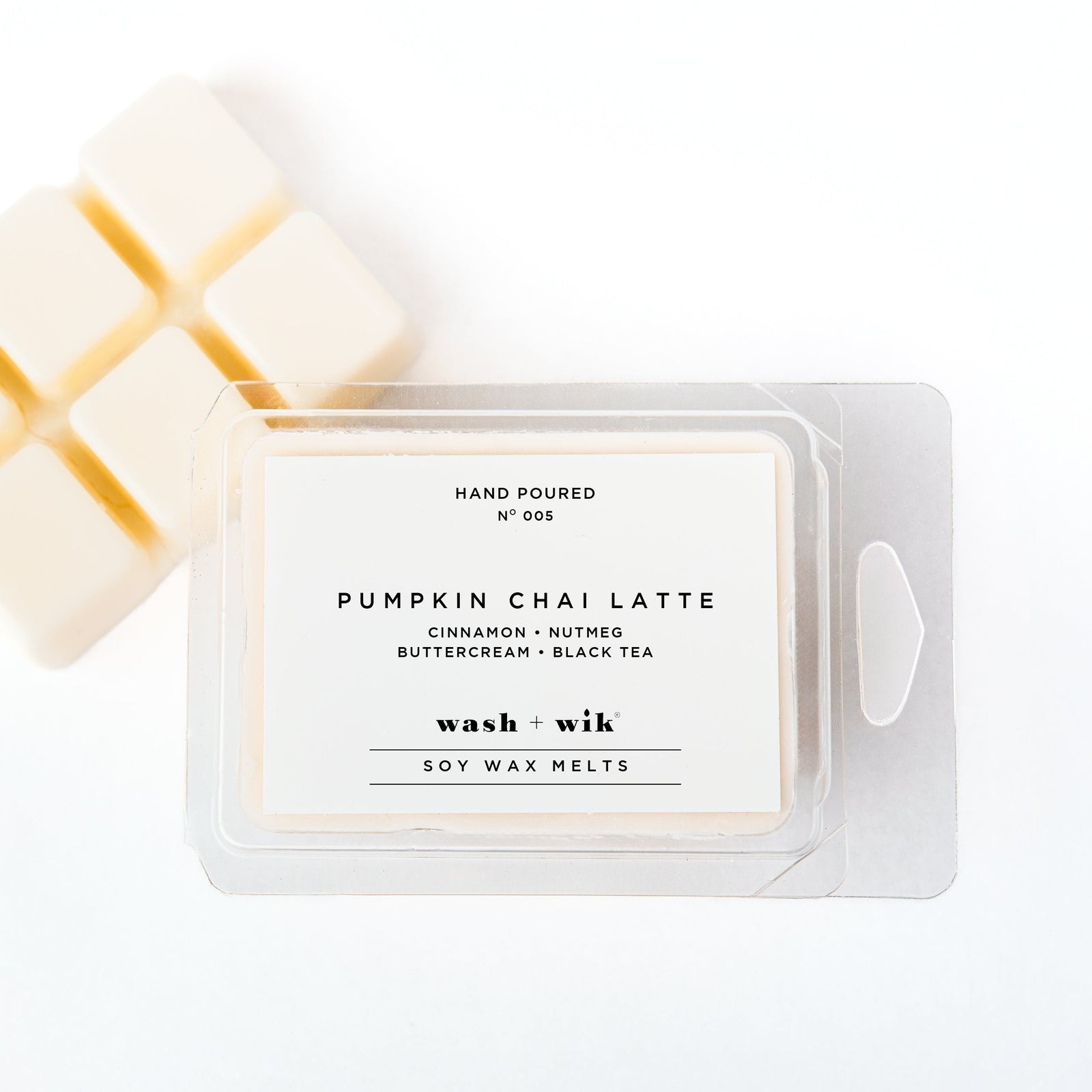 A clear plastic clamshell package of Wash + Wik soy wax melts on a white background, with several pale cream wax cubes partially visible behind it.