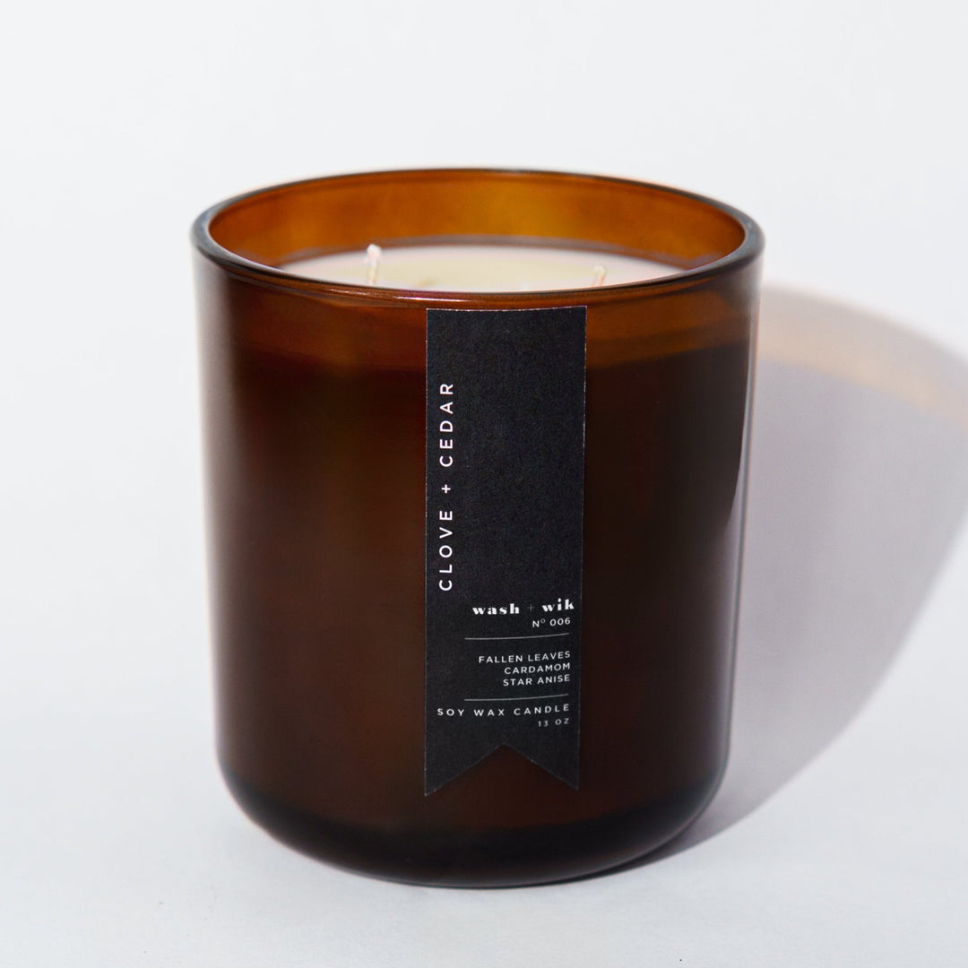 An amber glass jar candle with a black vertical label photographed on a clean white background with a soft shadow.