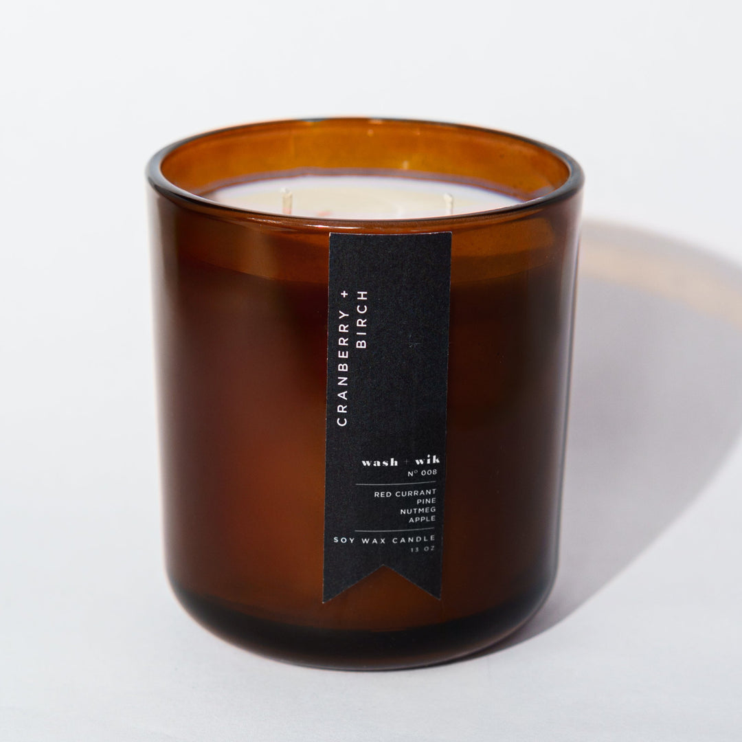 An amber glass jar candle with a black vertical label photographed on a clean white background with a soft shadow.