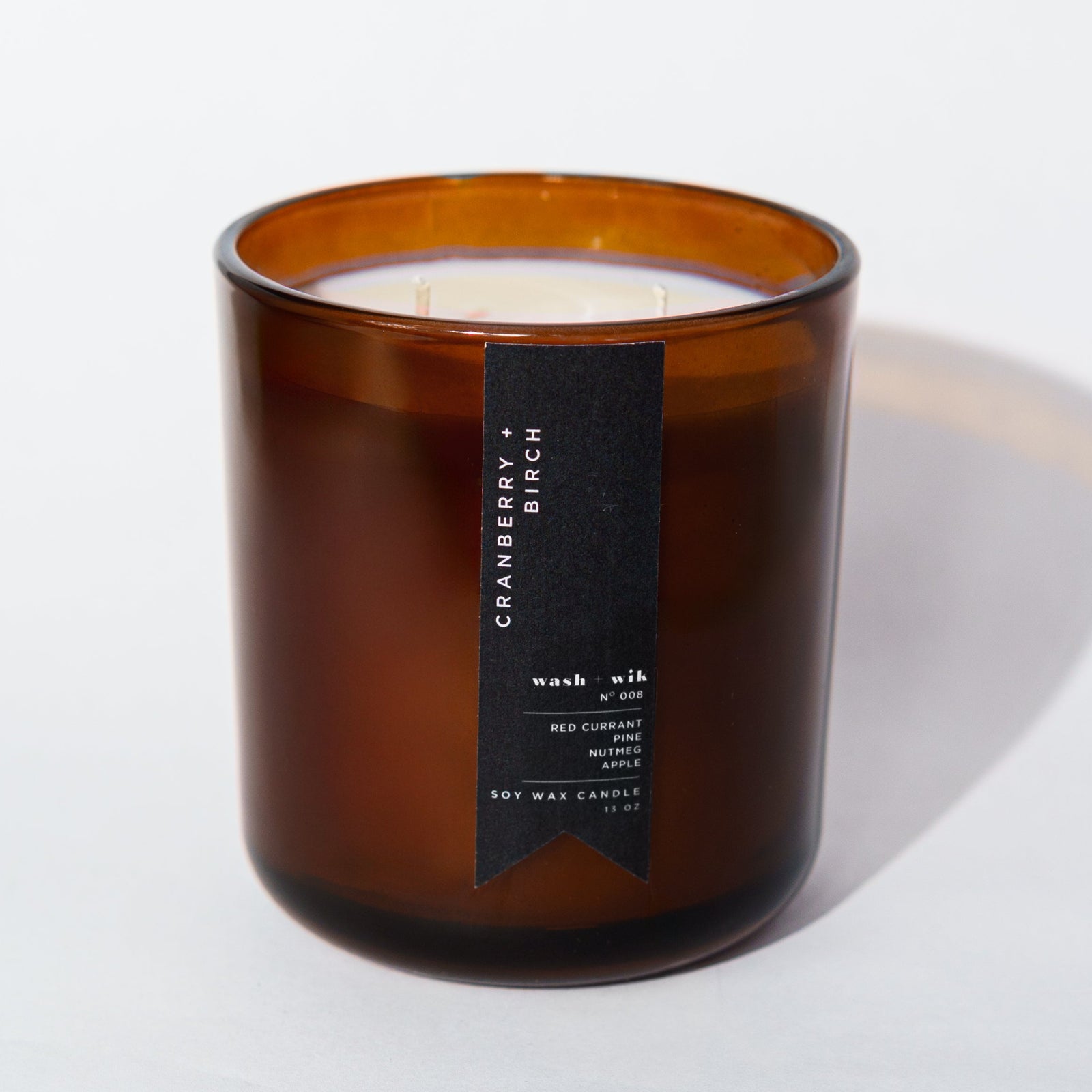 An amber glass jar candle with a black vertical label photographed on a clean white background with a soft shadow.