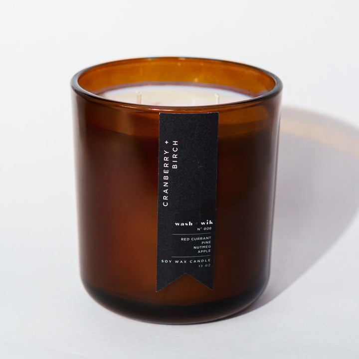 An amber glass jar candle with a black vertical label photographed on a clean white background with a soft shadow.