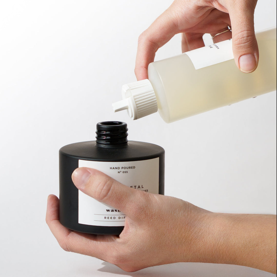 a hand pouring a refill bottle into a diffuser