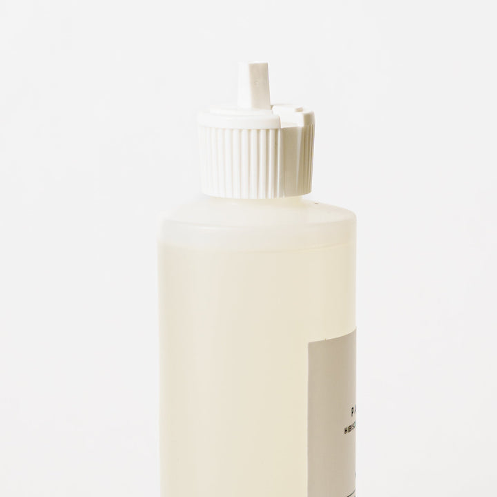 A bottle of Wash + Wik reed diffuser refill with a white cap and a minimalist white label, set against a clean white background with a soft shadow.
