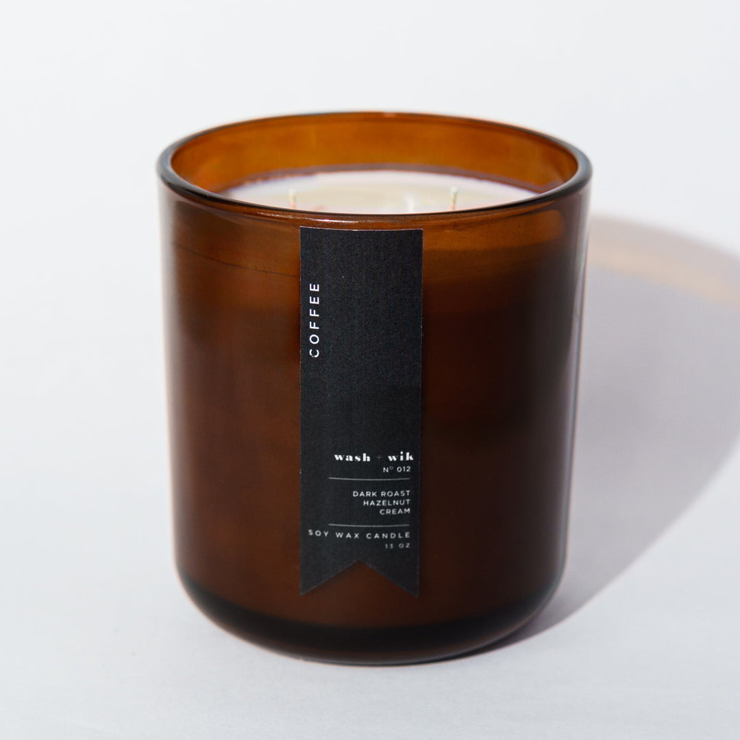 An amber glass jar candle with a black vertical label photographed on a clean white background with a soft shadow.