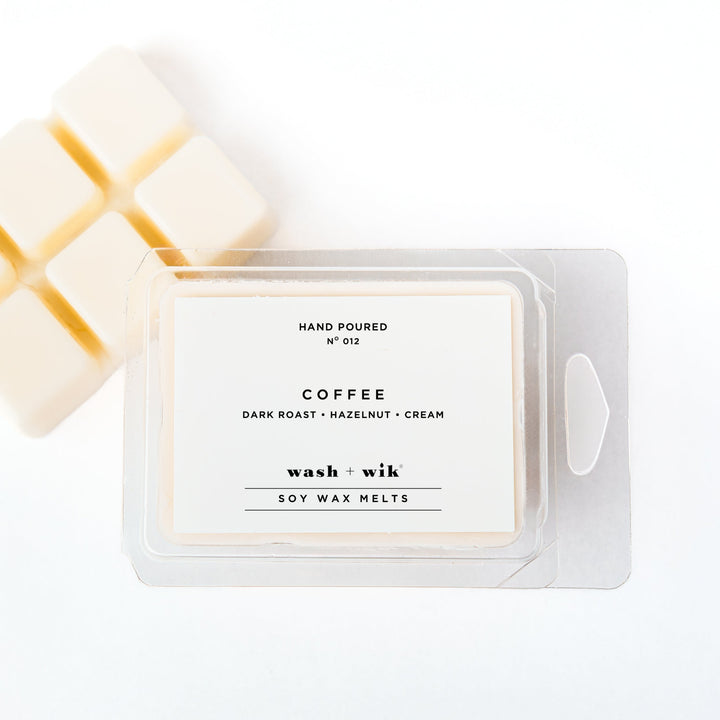 A clear plastic clamshell package of Wash + Wik soy wax melts on a white background, with several pale cream wax cubes partially visible behind it.