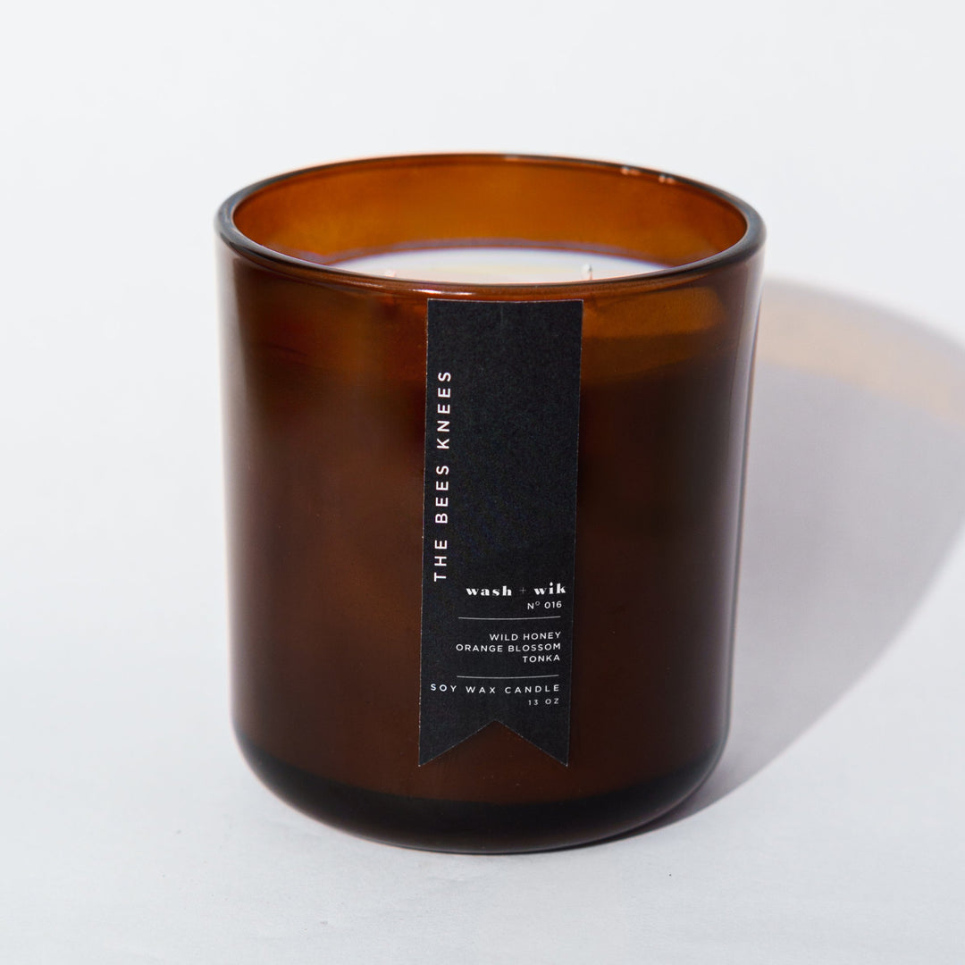 An amber glass jar candle with a black vertical label photographed on a clean white background with a soft shadow.
