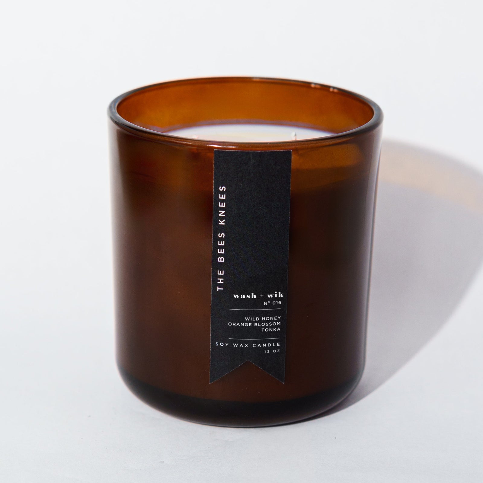 An amber glass jar candle with a black vertical label photographed on a clean white background with a soft shadow.
