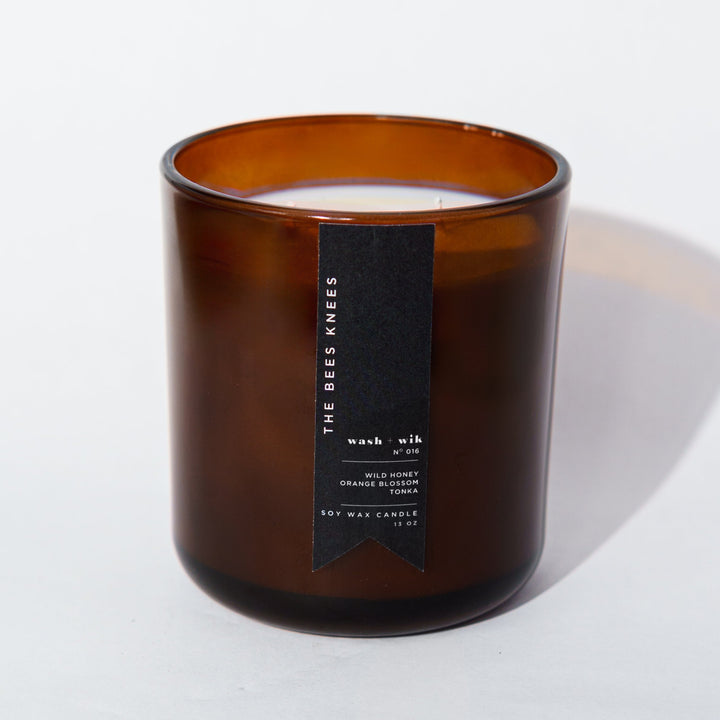 An amber glass jar candle with a black vertical label photographed on a clean white background with a soft shadow.
