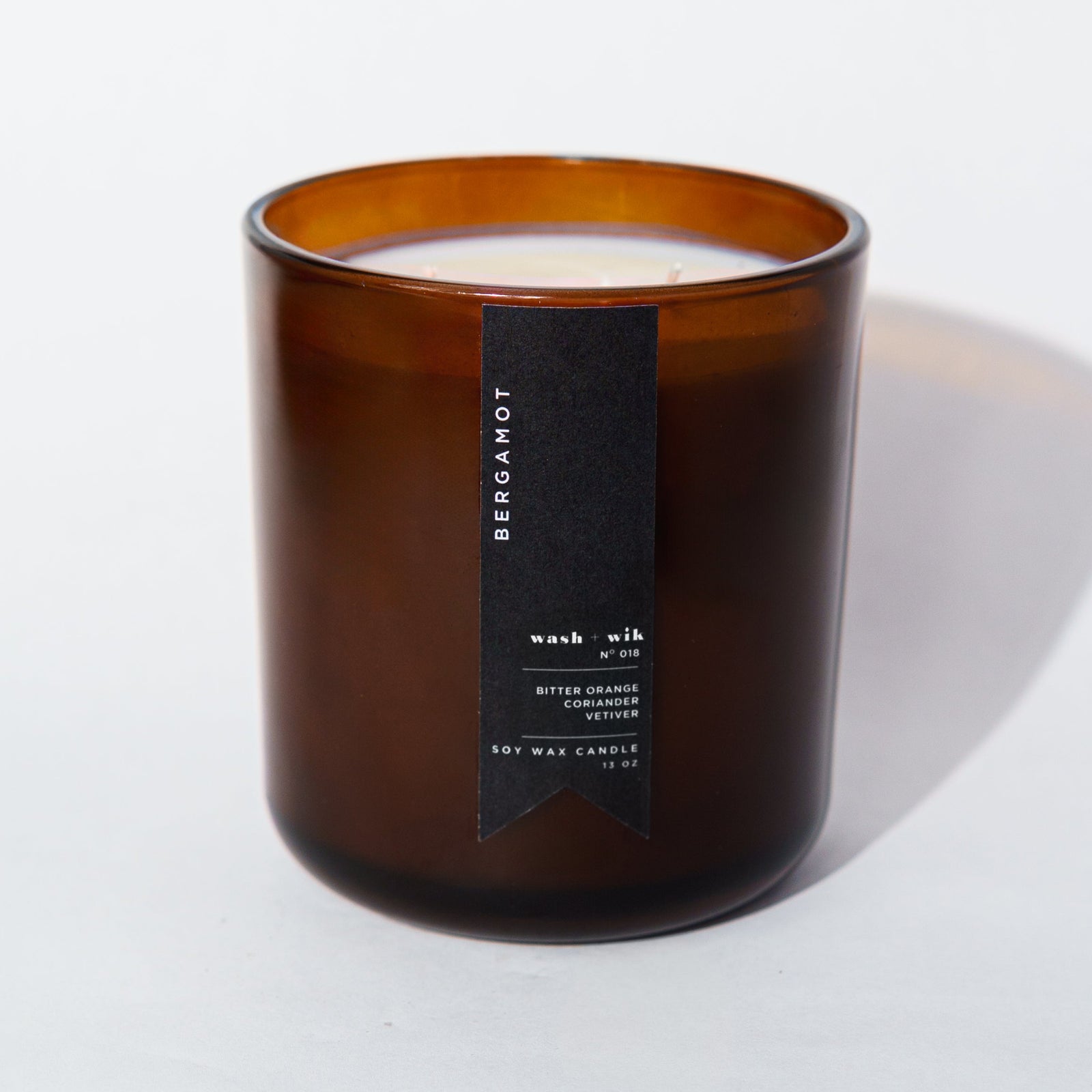 An amber glass jar candle with a black vertical label photographed on a clean white background with a soft shadow.