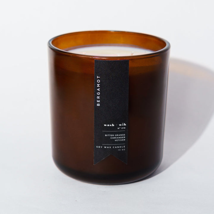 An amber glass jar candle with a black vertical label photographed on a clean white background with a soft shadow.