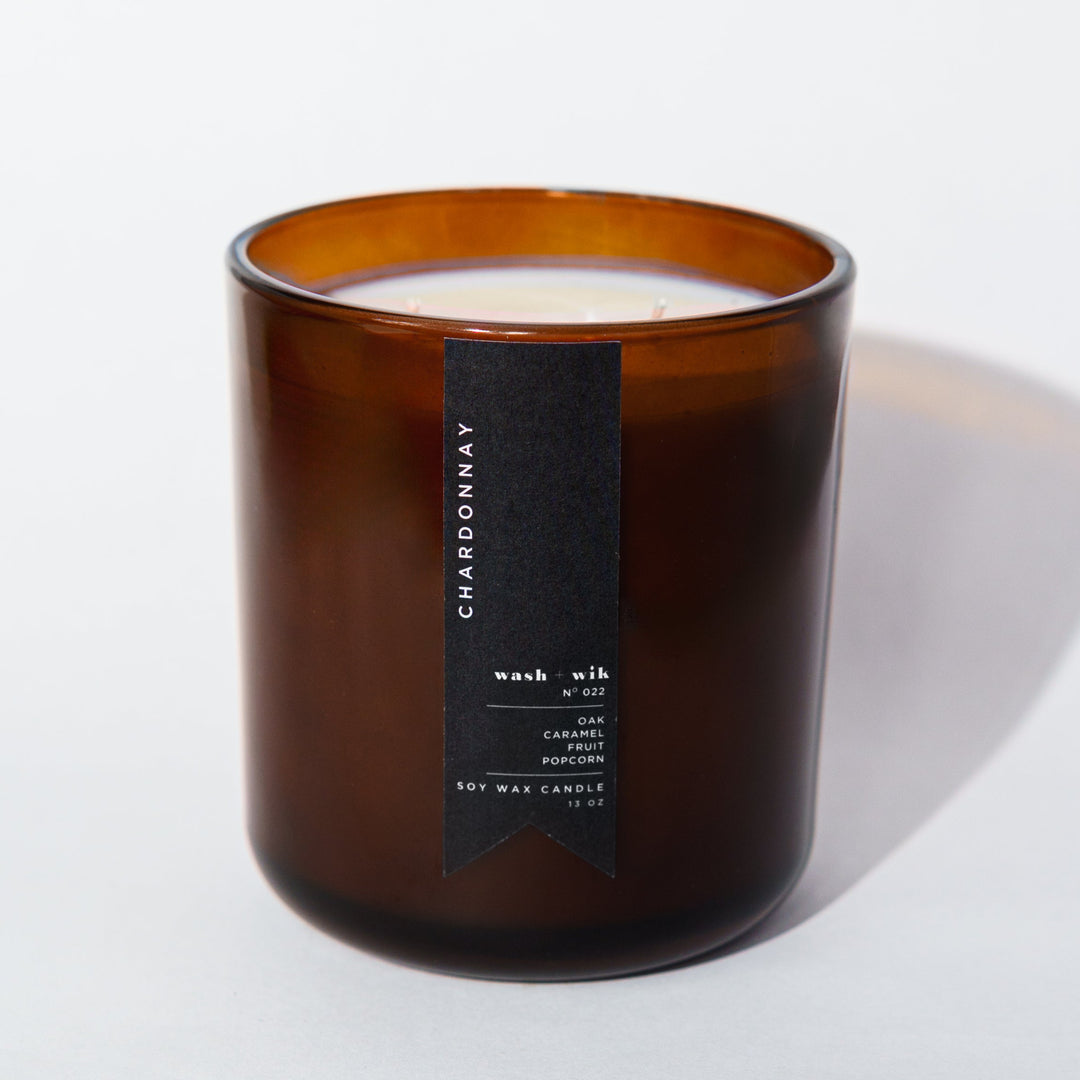An amber glass jar candle with a black vertical label photographed on a clean white background with a soft shadow.