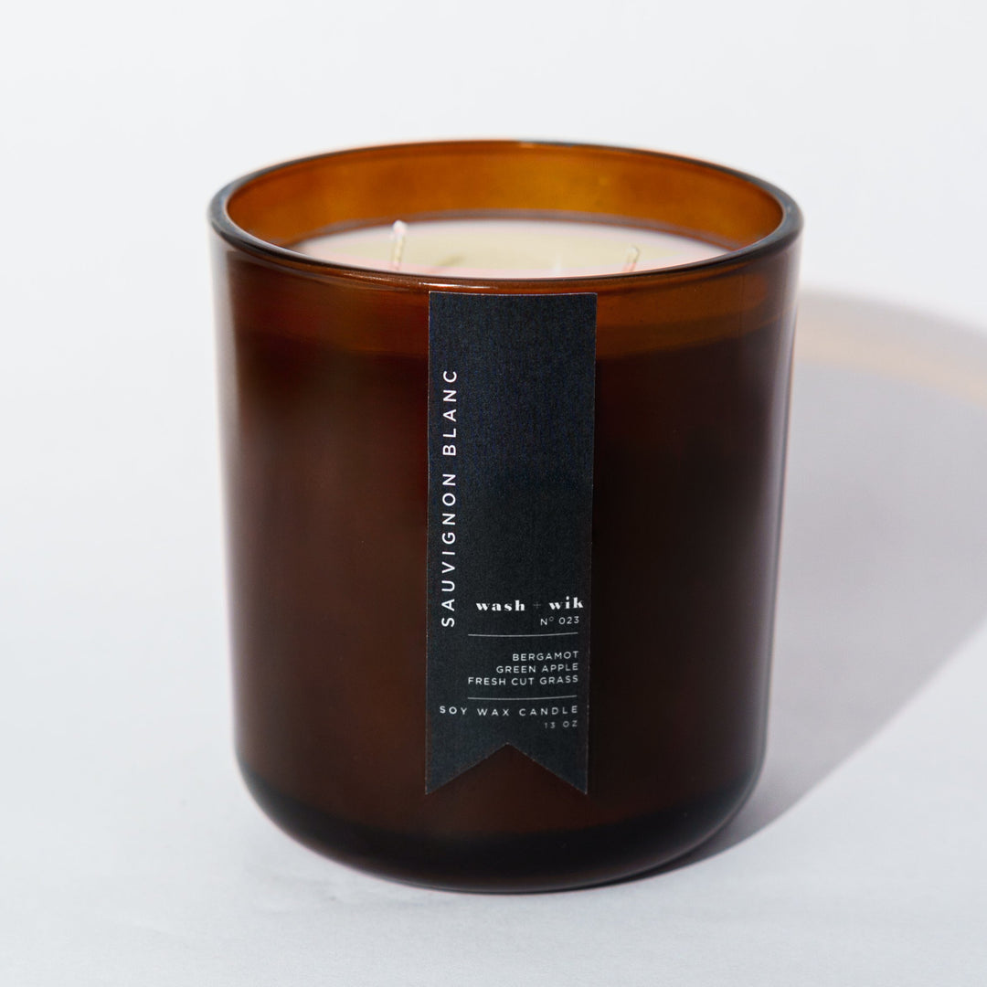 An amber glass jar candle with a black vertical label photographed on a clean white background with a soft shadow.