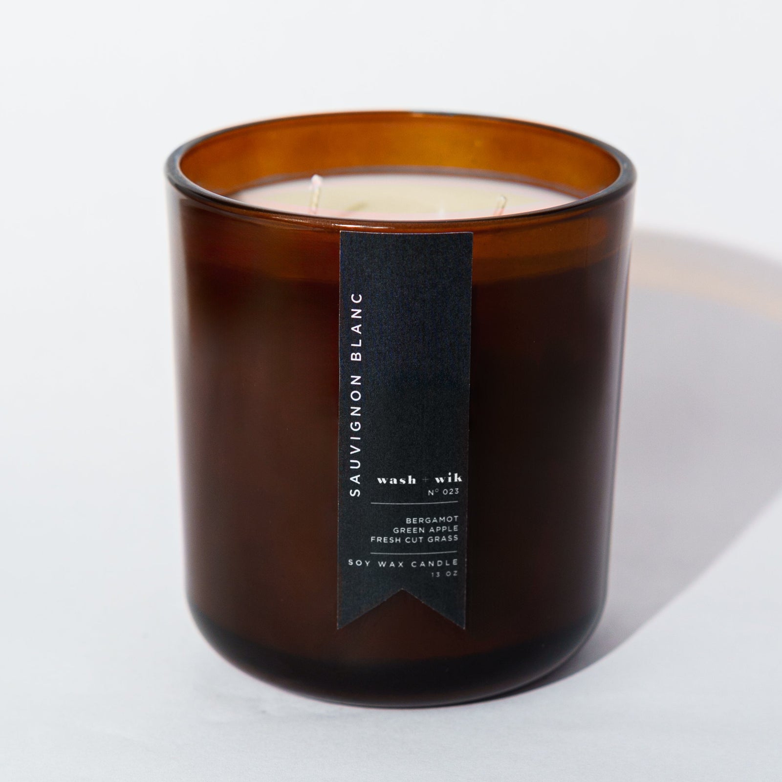 An amber glass jar candle with a black vertical label photographed on a clean white background with a soft shadow.
