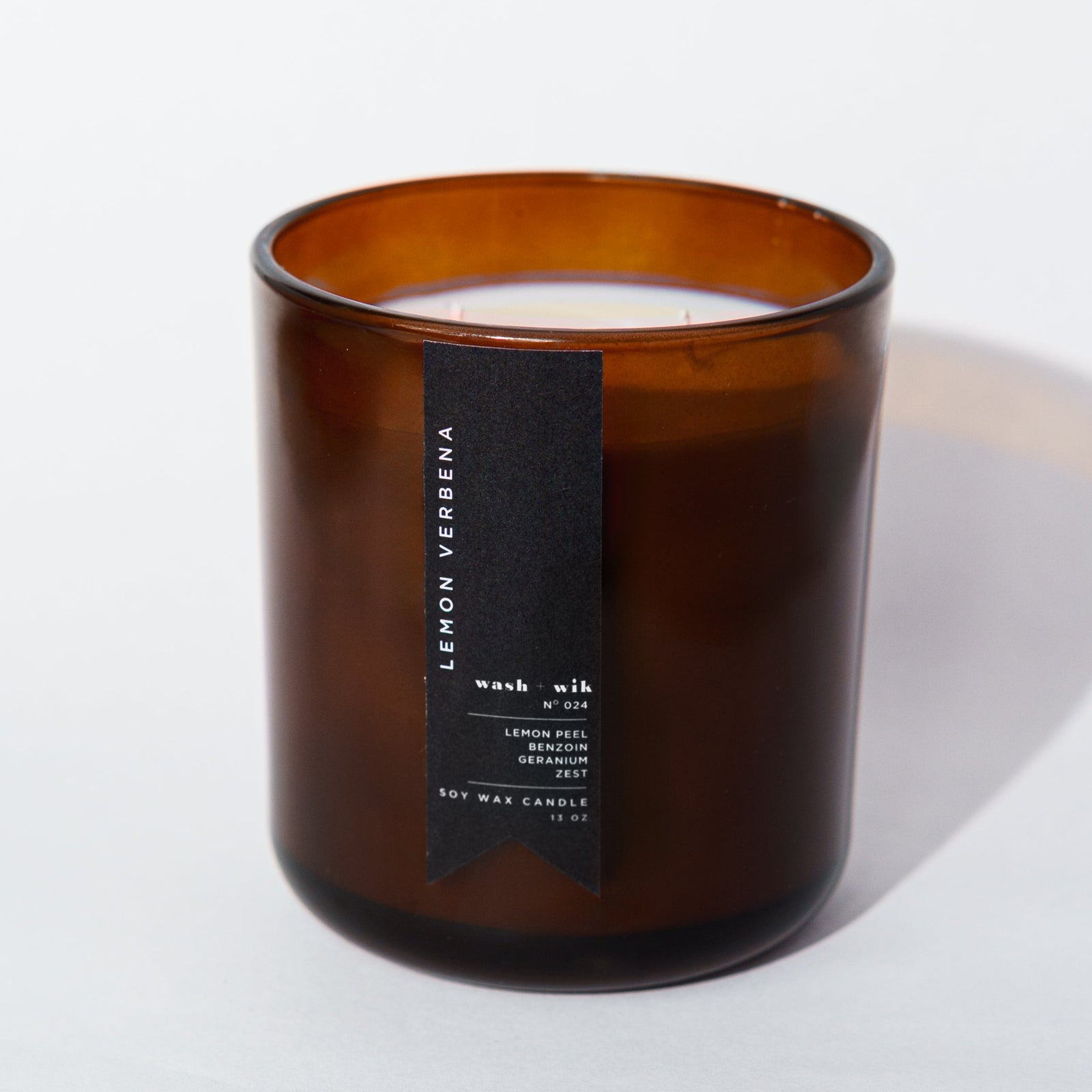 An amber glass jar candle with a black vertical label photographed on a clean white background with a soft shadow.
