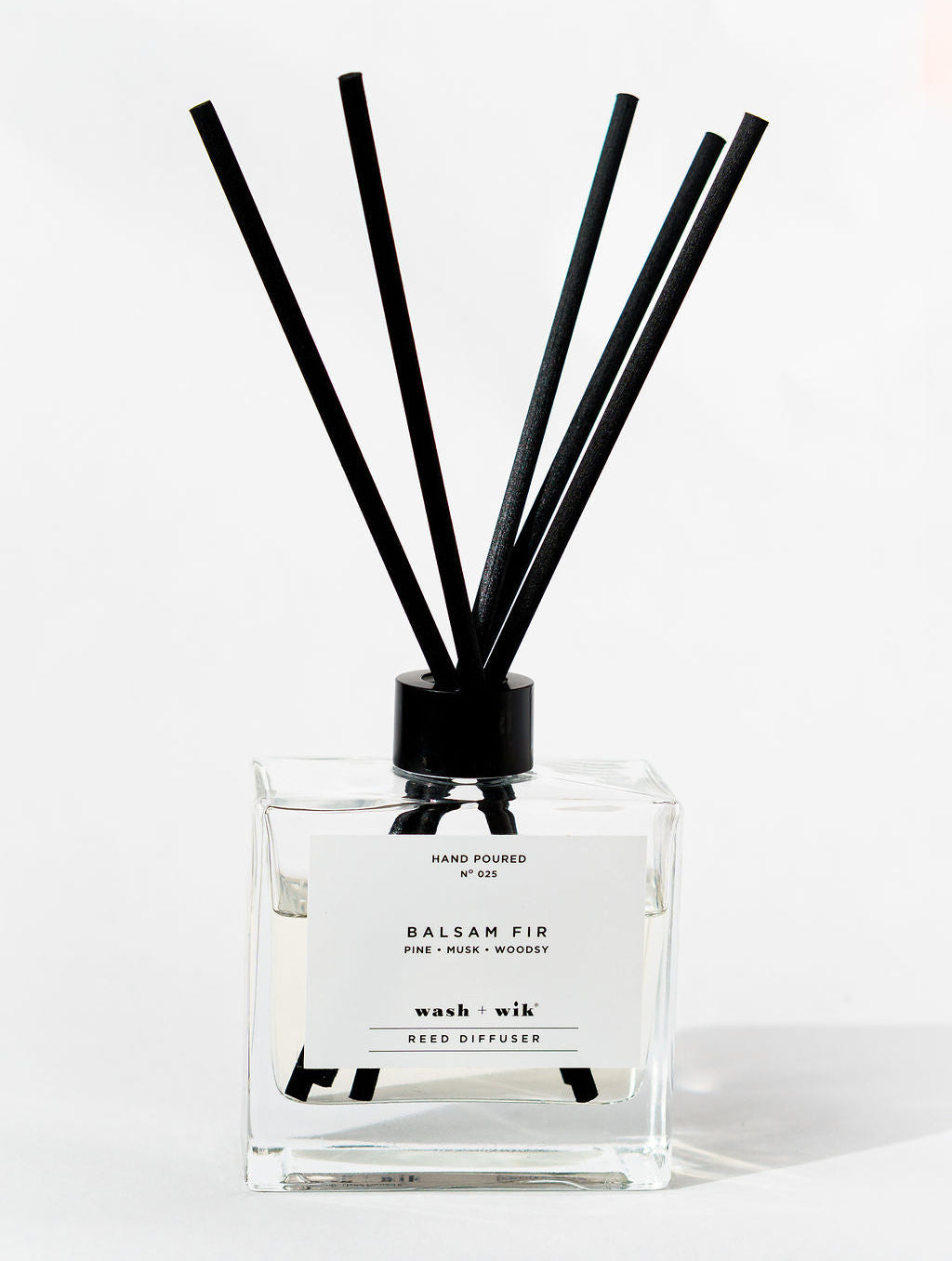 Reed diffuser with black sticks in a clear bottle on a white background