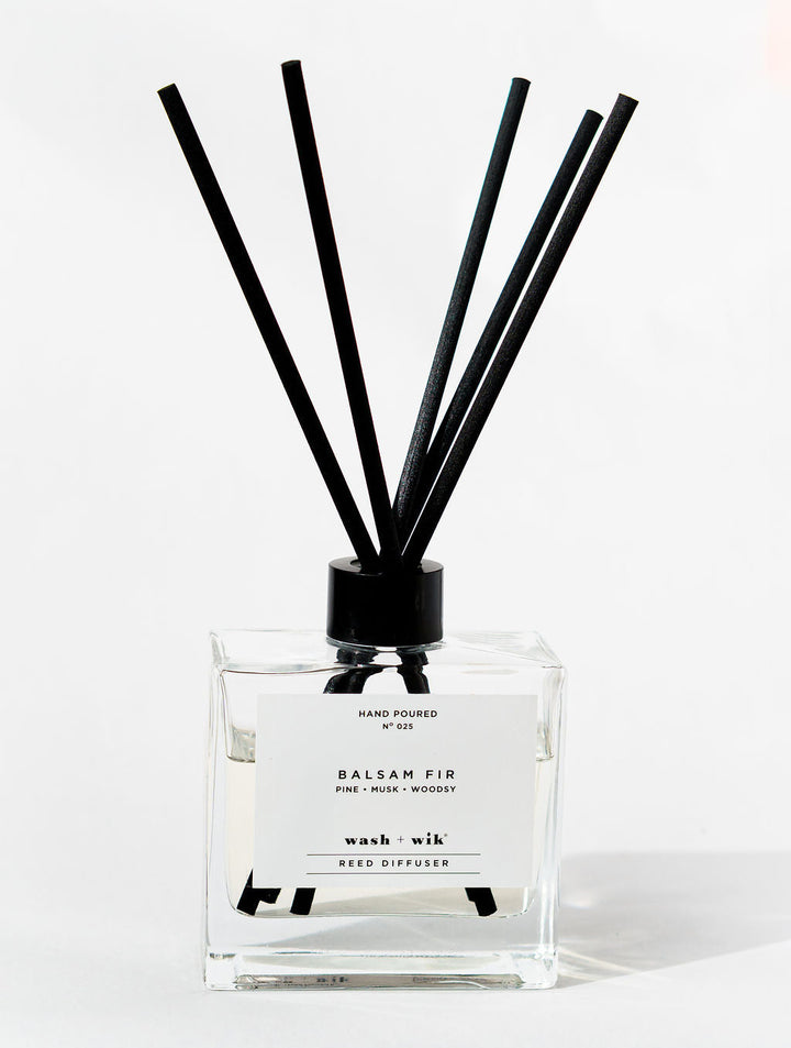 Reed diffuser with black sticks in a clear bottle on a white background