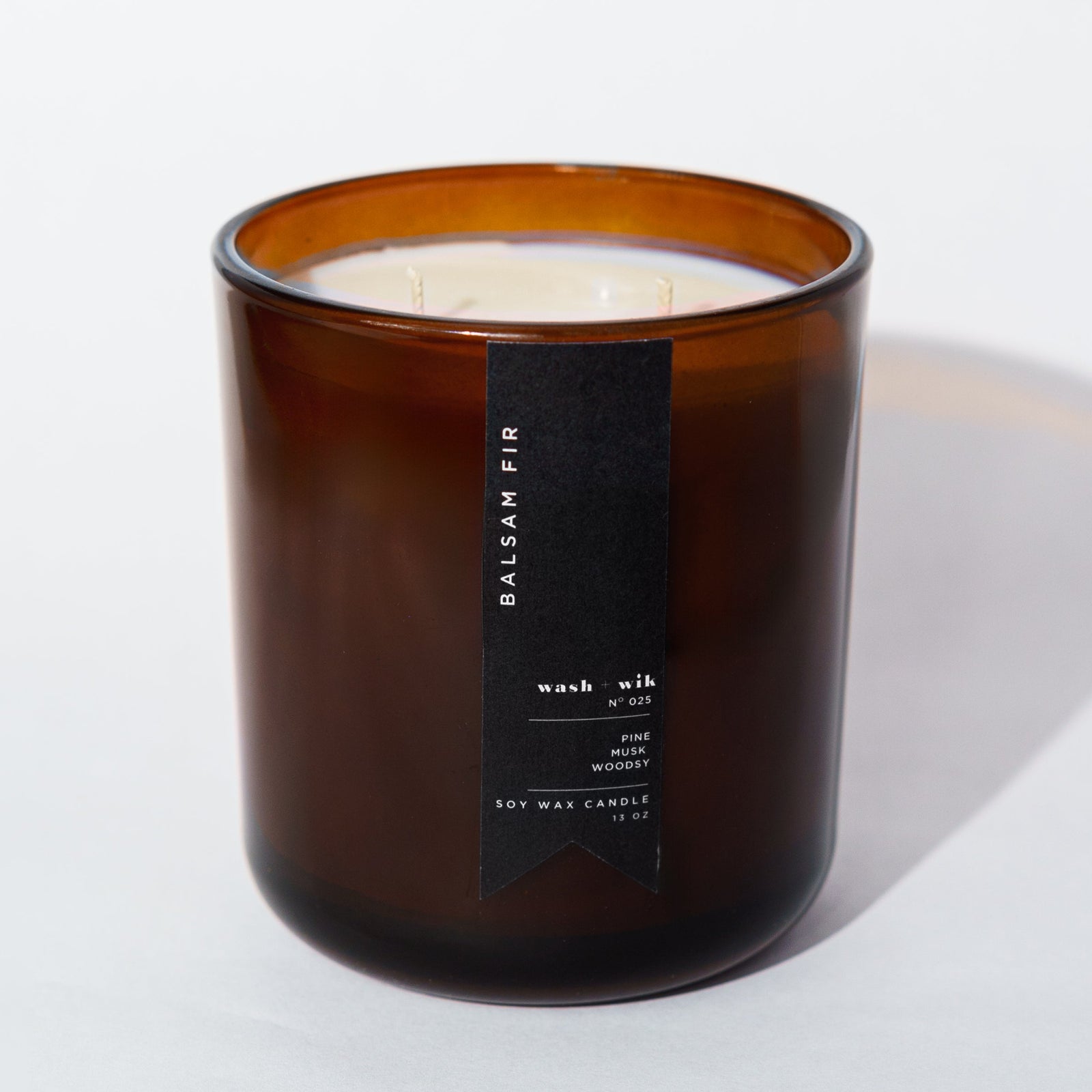 An amber glass jar candle with a black vertical label photographed on a clean white background with a soft shadow.