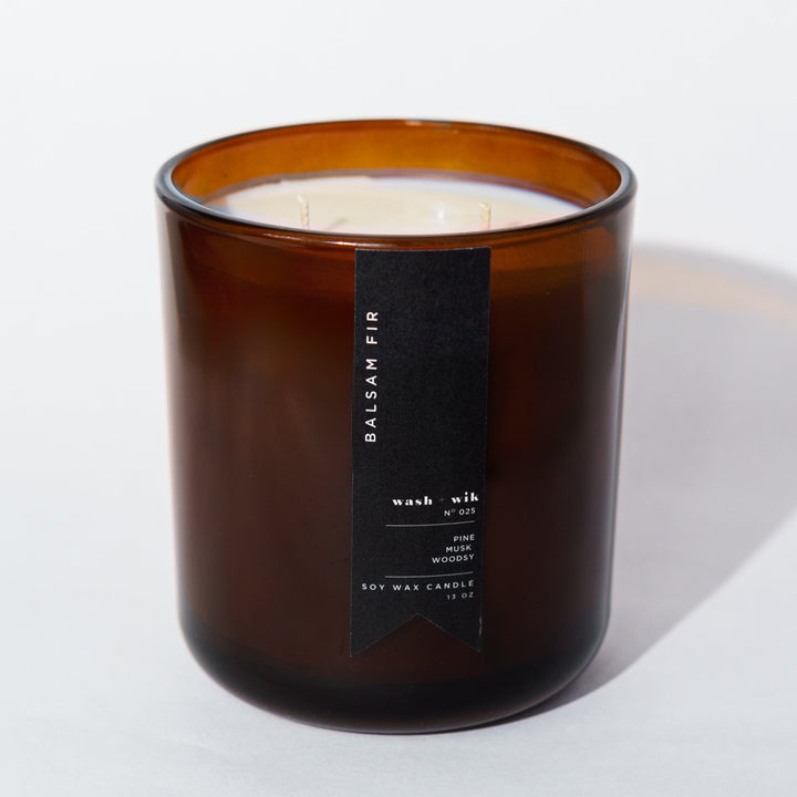 An amber glass jar candle with a black vertical label photographed on a clean white background with a soft shadow.