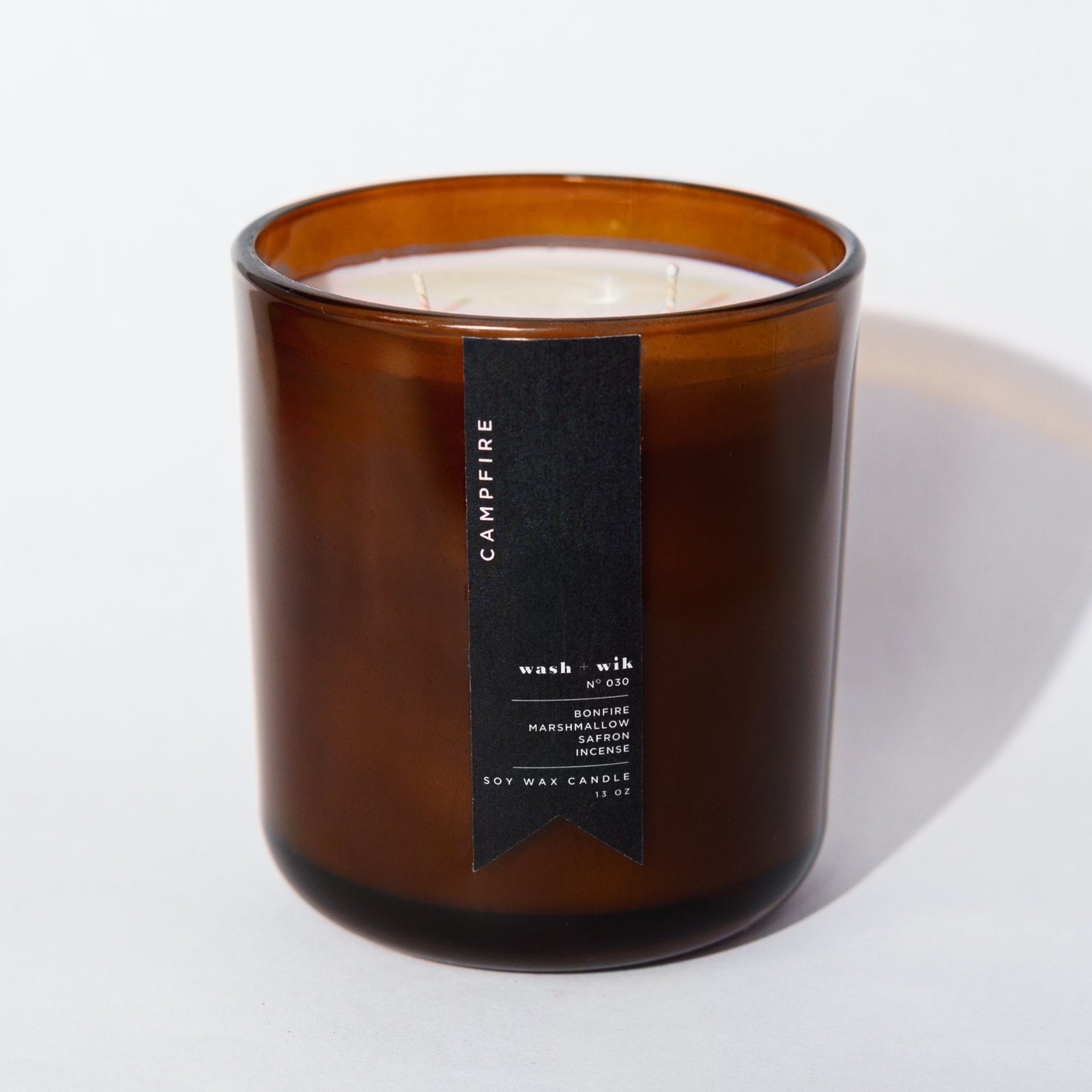 An amber glass jar candle with a black vertical label photographed on a clean white background with a soft shadow.