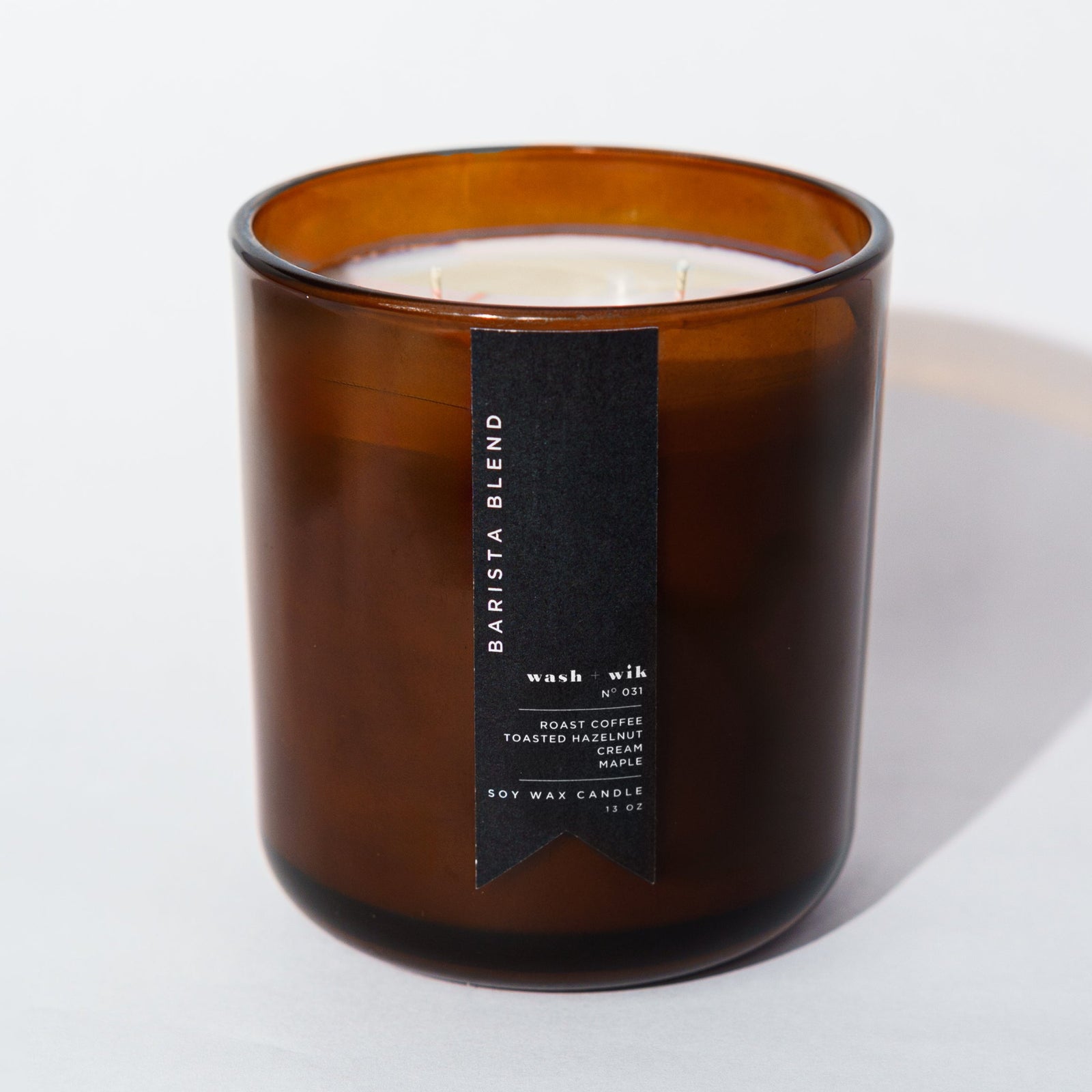 An amber glass jar candle with a black vertical label photographed on a clean white background with a soft shadow.