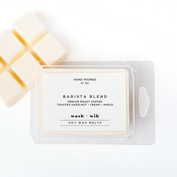 A clear plastic clamshell package of Wash + Wik soy wax melts on a white background, with several pale cream wax cubes partially visible behind it.