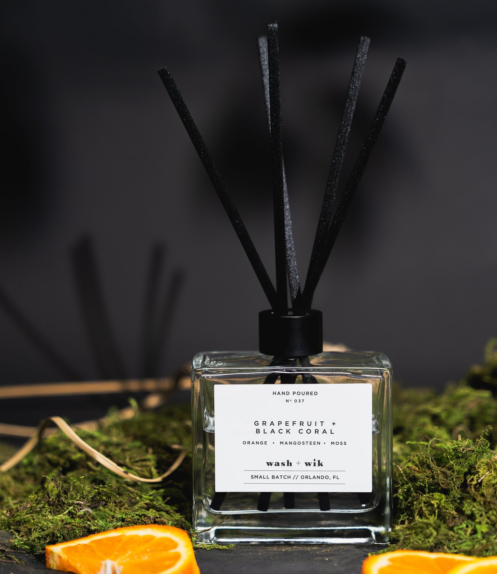 Reed diffuser with black sticks on a dark background with oranges