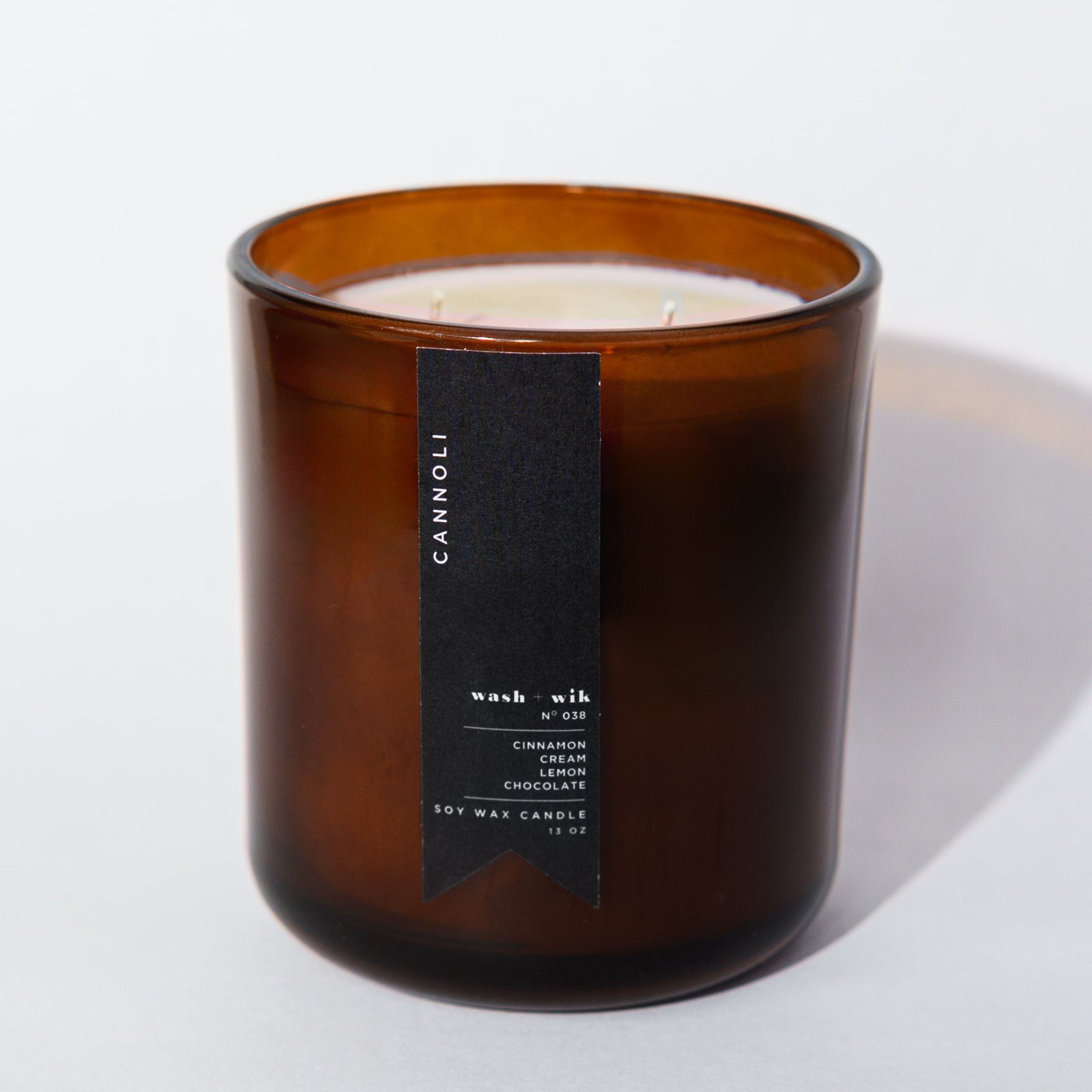 An amber glass jar candle with a black vertical label photographed on a clean white background with a soft shadow.