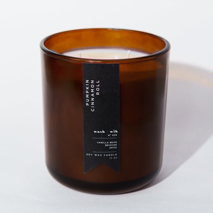 An amber glass jar candle with a black vertical label photographed on a clean white background with a soft shadow.