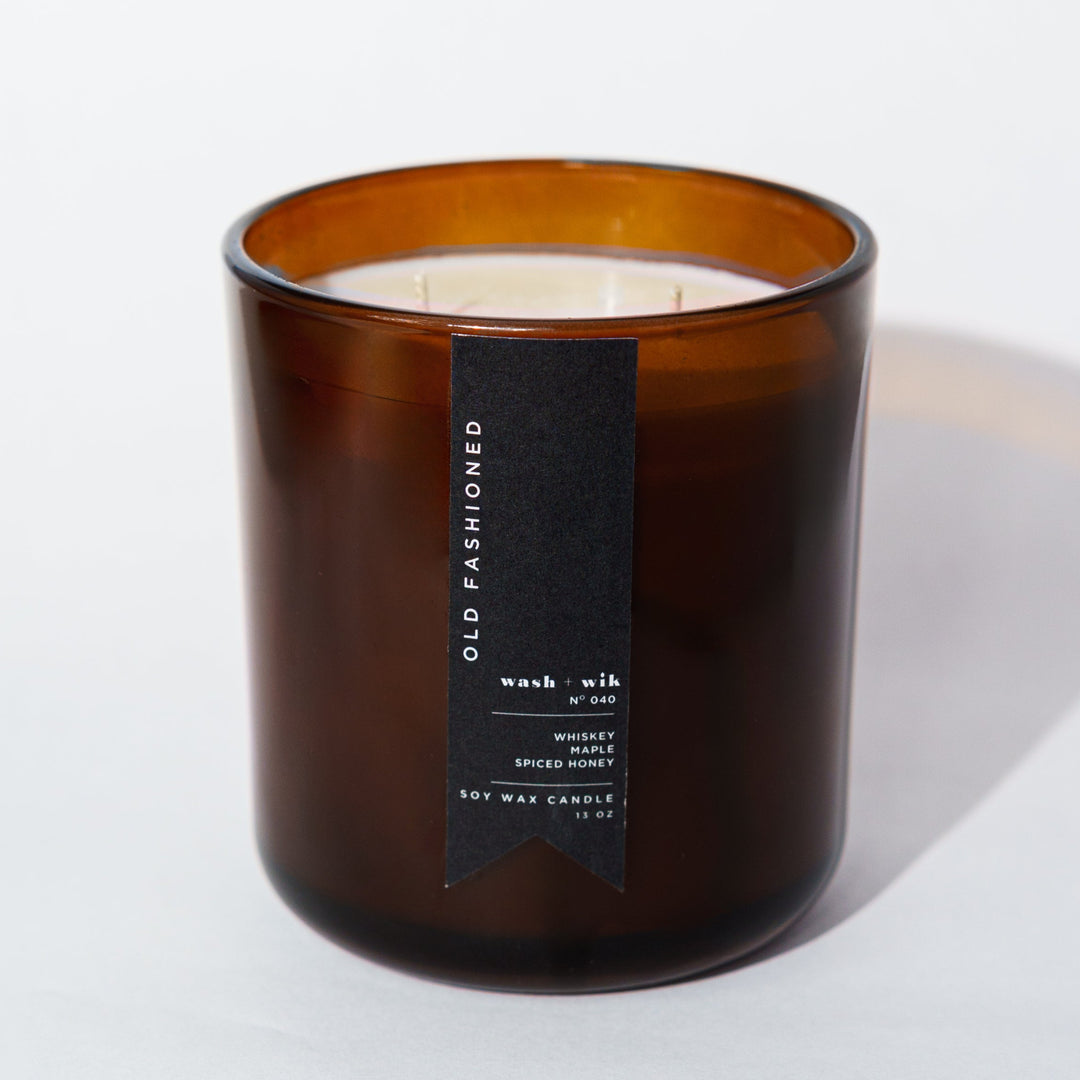 An amber glass jar candle with a black vertical label photographed on a clean white background with a soft shadow.