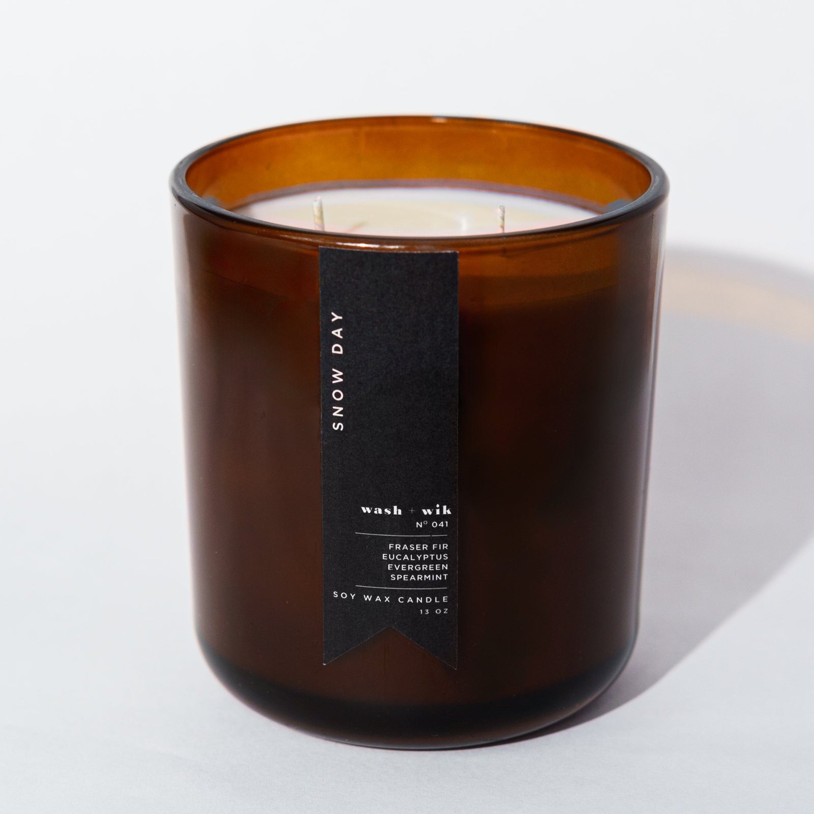 An amber glass jar candle with a black vertical label photographed on a clean white background with a soft shadow.