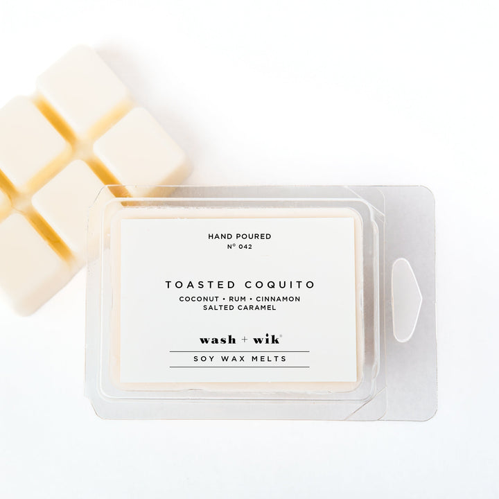 A clear plastic clamshell package of Wash + Wik soy wax melts on a white background, with several pale cream wax cubes partially visible behind it.