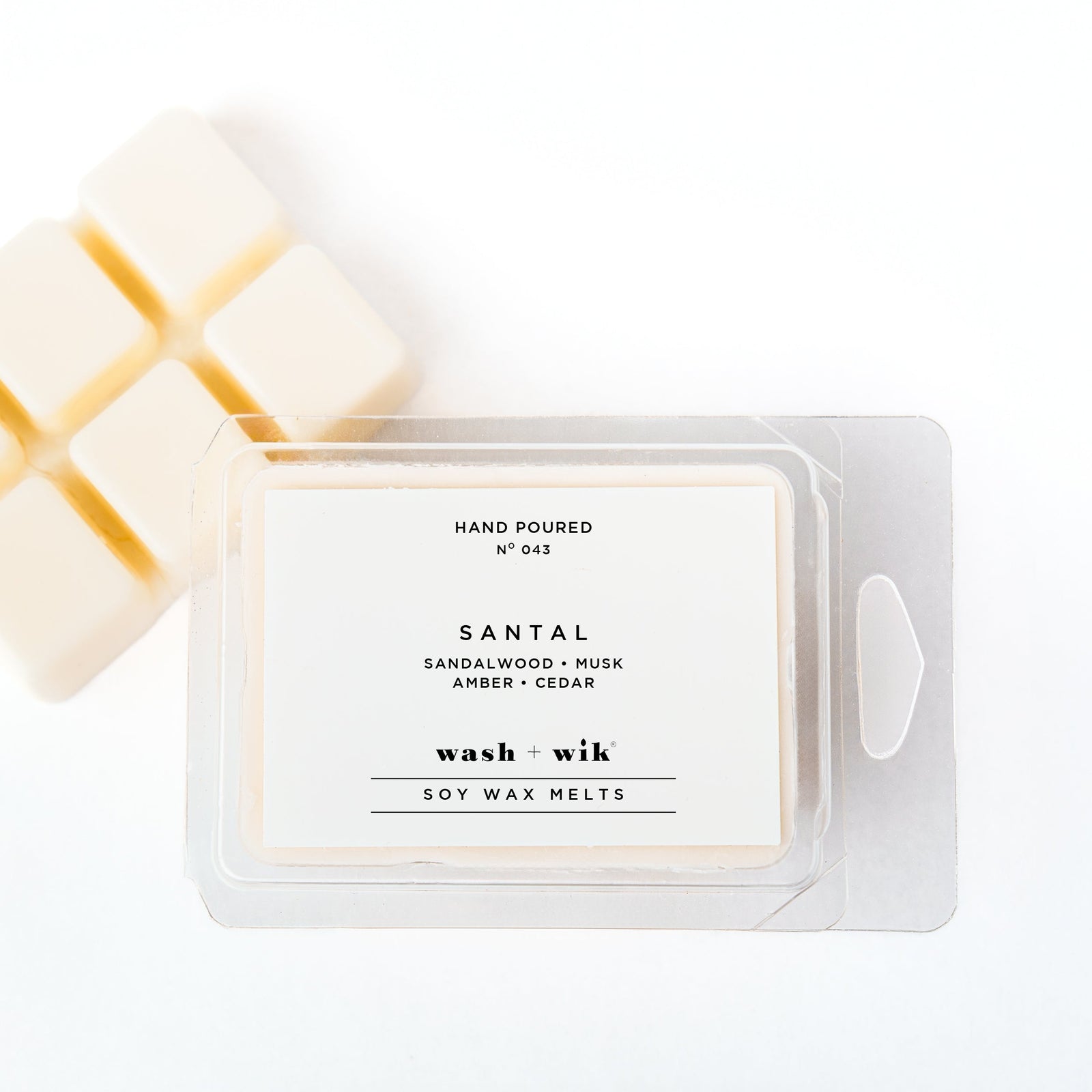 A clear plastic clamshell package of Wash + Wik soy wax melts on a white background, with several pale cream wax cubes partially visible behind it.