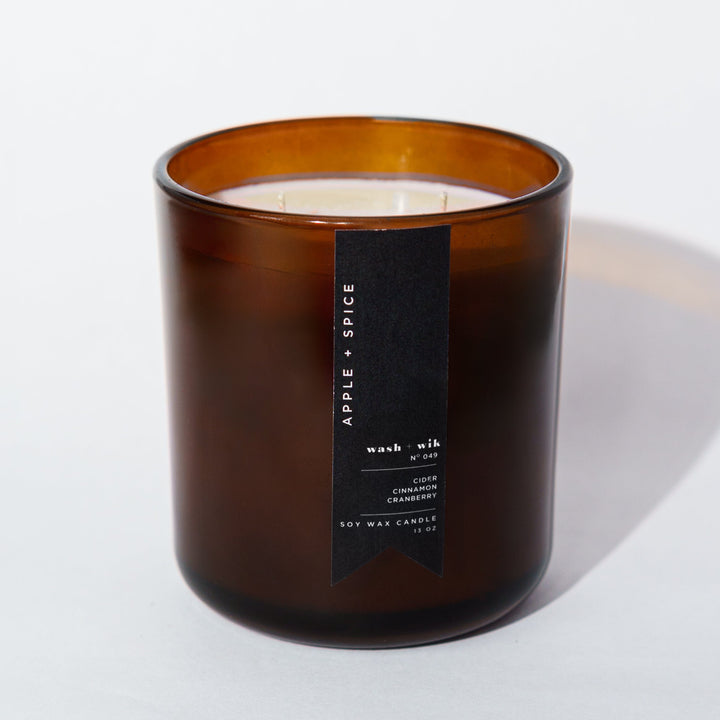 An amber glass jar candle with a black vertical label photographed on a clean white background with a soft shadow.