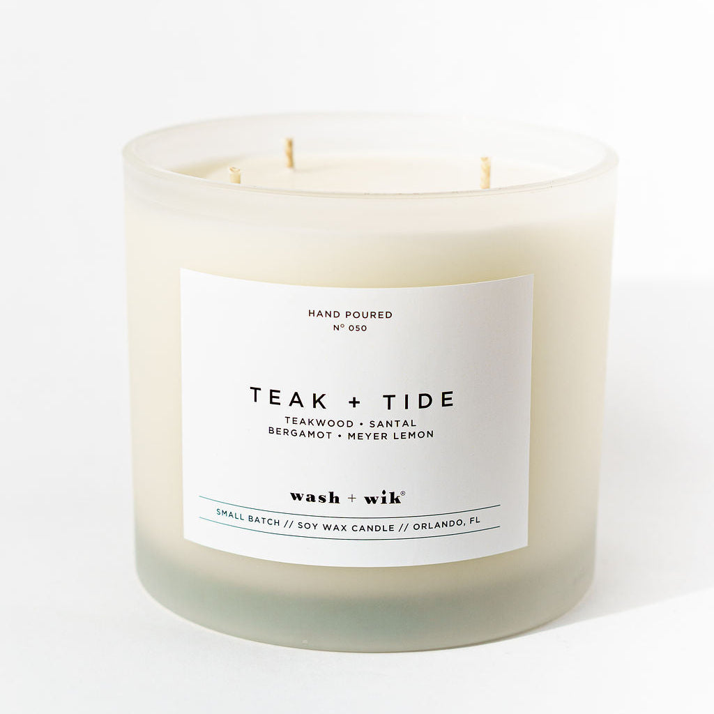 Candle labeled 'Teak + Tide' with a white label on a white background