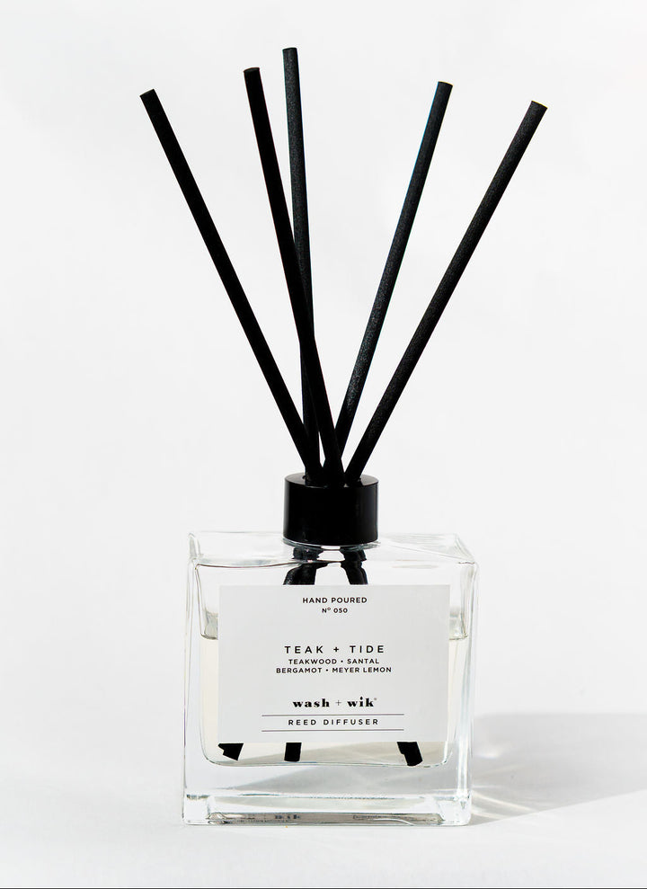 Reed diffuser with black sticks in a clear bottle on a white background