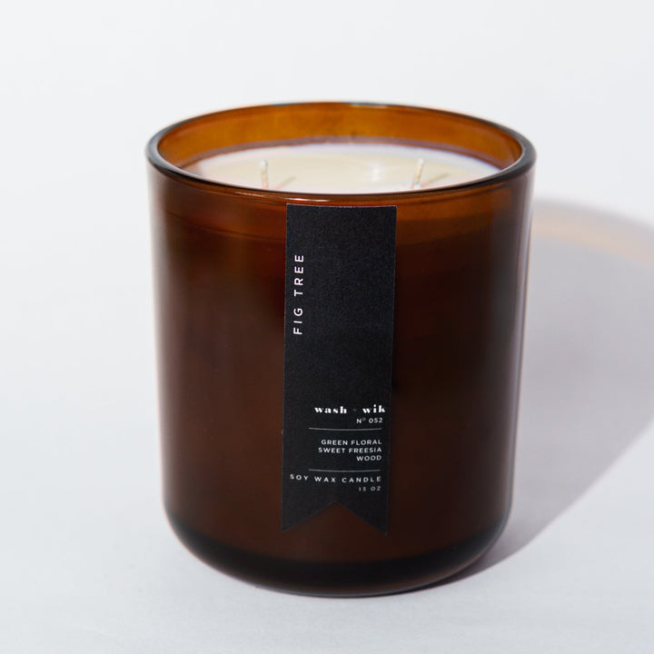 An amber glass jar candle with a black vertical label photographed on a clean white background with a soft shadow.