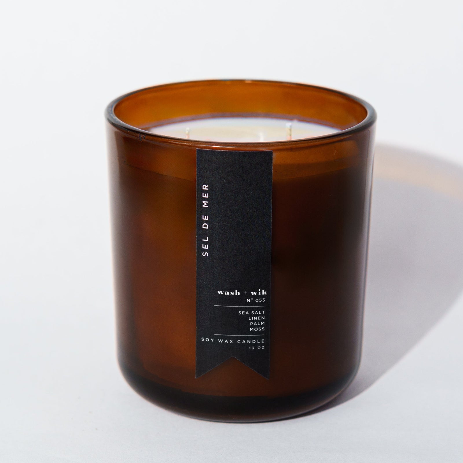An amber glass jar candle with a black vertical label photographed on a clean white background with a soft shadow.