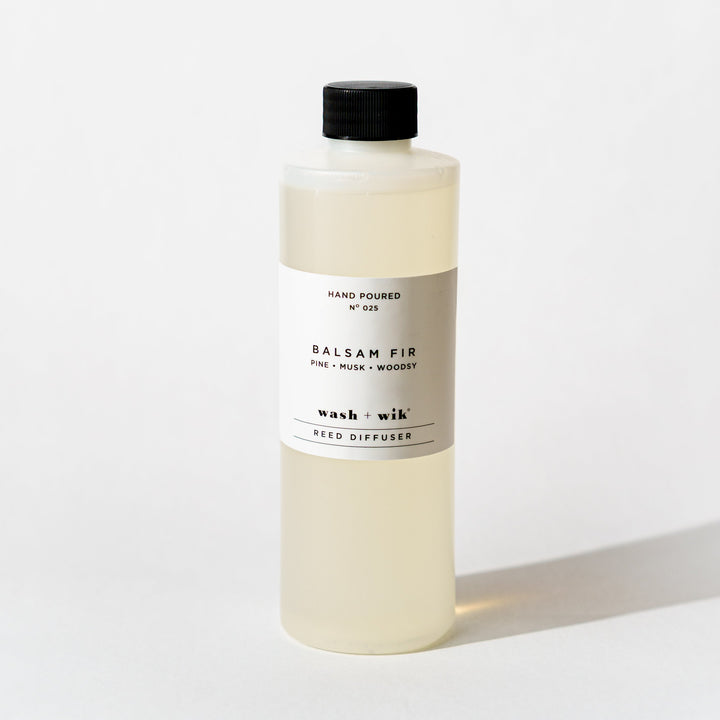 A bottle of Wash + Wik reed diffuser refill with a black cap and a minimalist white label, set against a clean white background with a soft shadow.