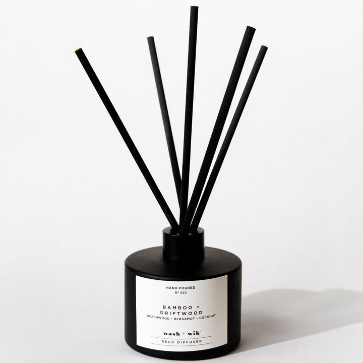 A black reed diffuser bottle with a black cap and five black reeds