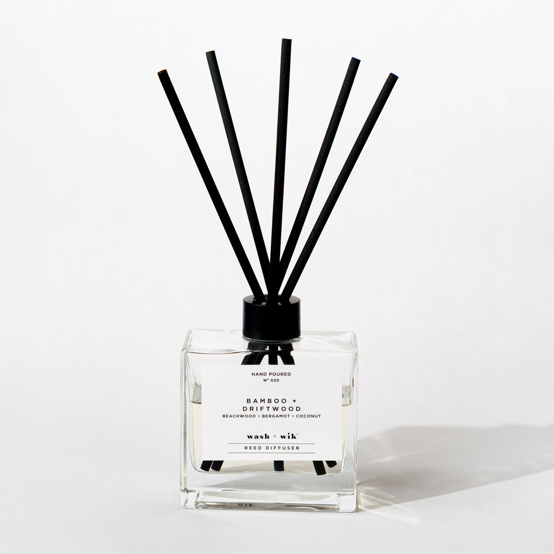 A clear glass reed diffuser bottle with a black cap and five black reeds