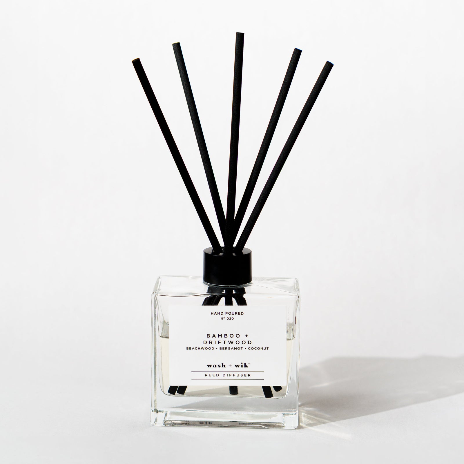 A clear glass reed diffuser bottle with a black cap and five black reeds