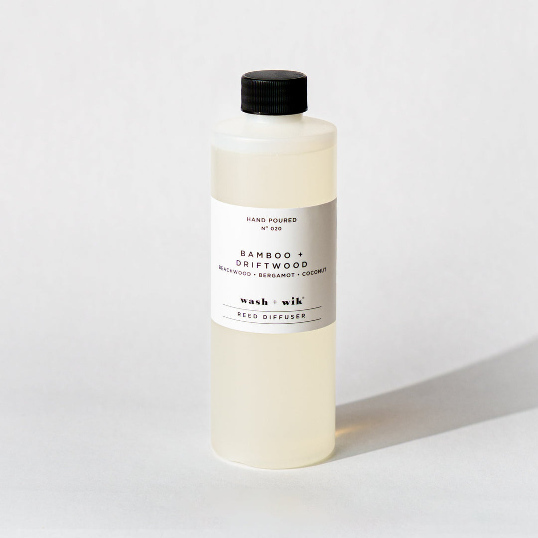 A bottle of Wash + Wik reed diffuser refill with a black cap and a minimalist white label, set against a clean white background with a soft shadow.