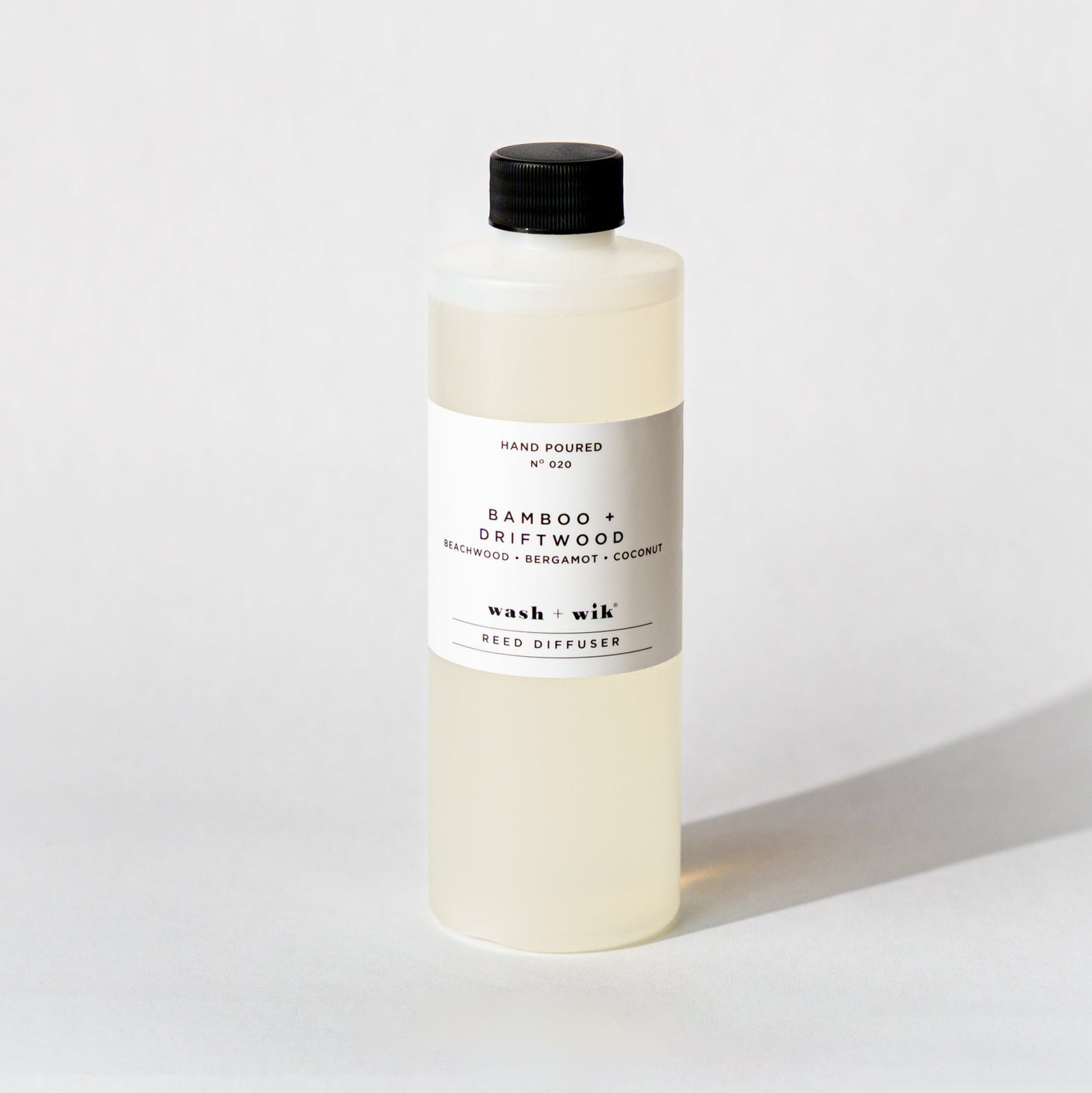 A bottle of Wash + Wik reed diffuser refill with a black cap and a minimalist white label, set against a clean white background with a soft shadow.