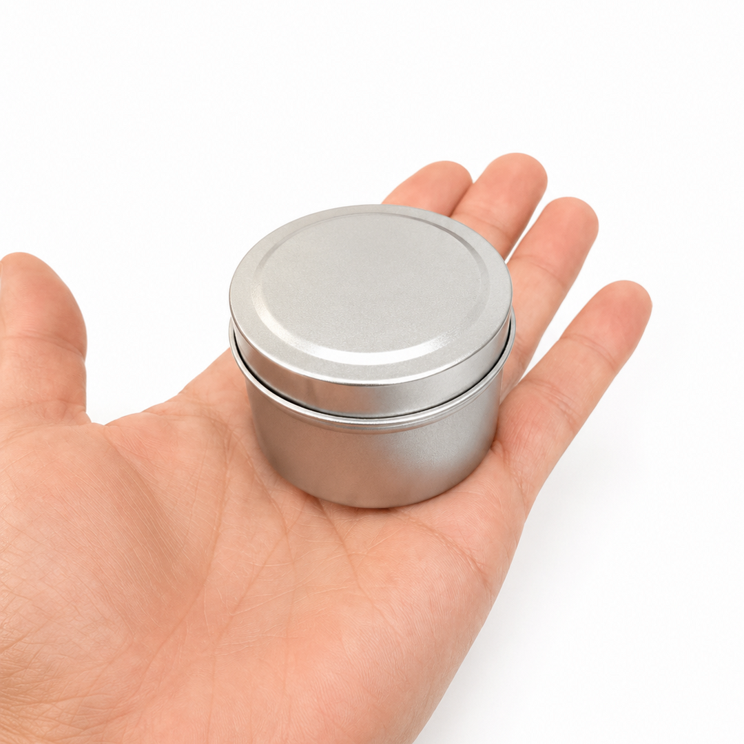 A small round silver metal tin with a matching lid, held in the palm of a hand against a plain white background.