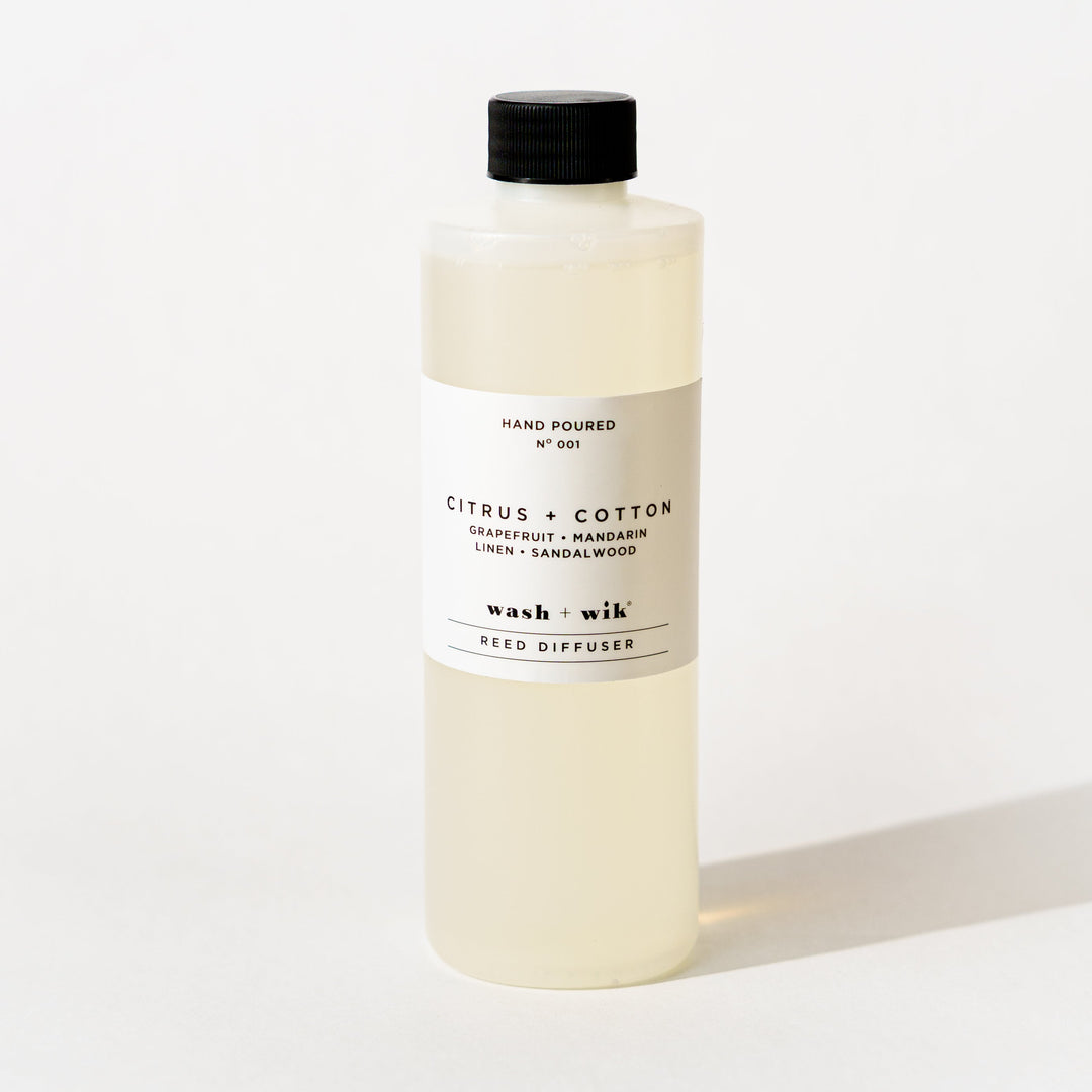 A bottle of Wash + Wik reed diffuser refill with a black cap and a minimalist white label, set against a clean white background with a soft shadow.