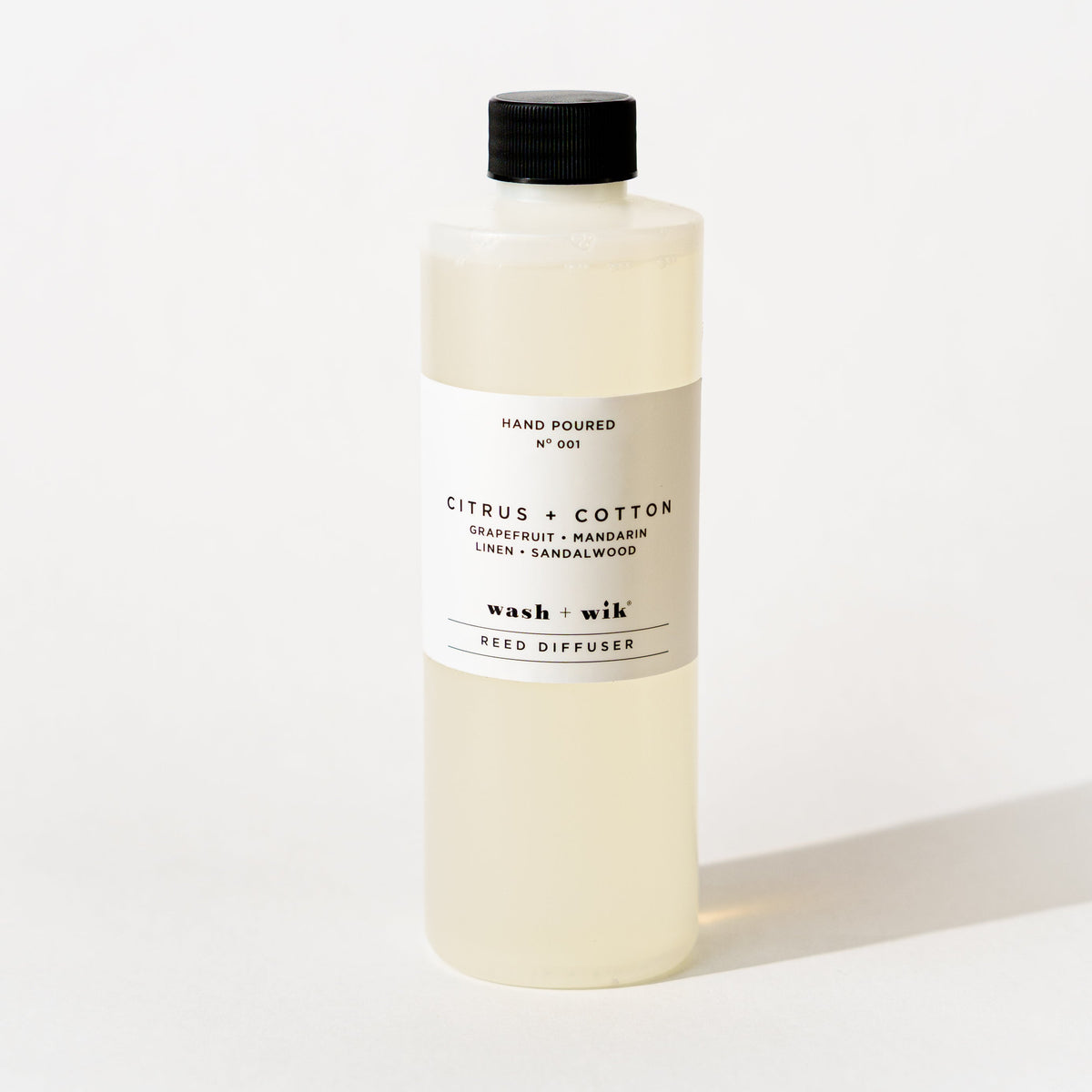 A bottle of Wash + Wik reed diffuser refill with a black cap and a minimalist white label, set against a clean white background with a soft shadow.