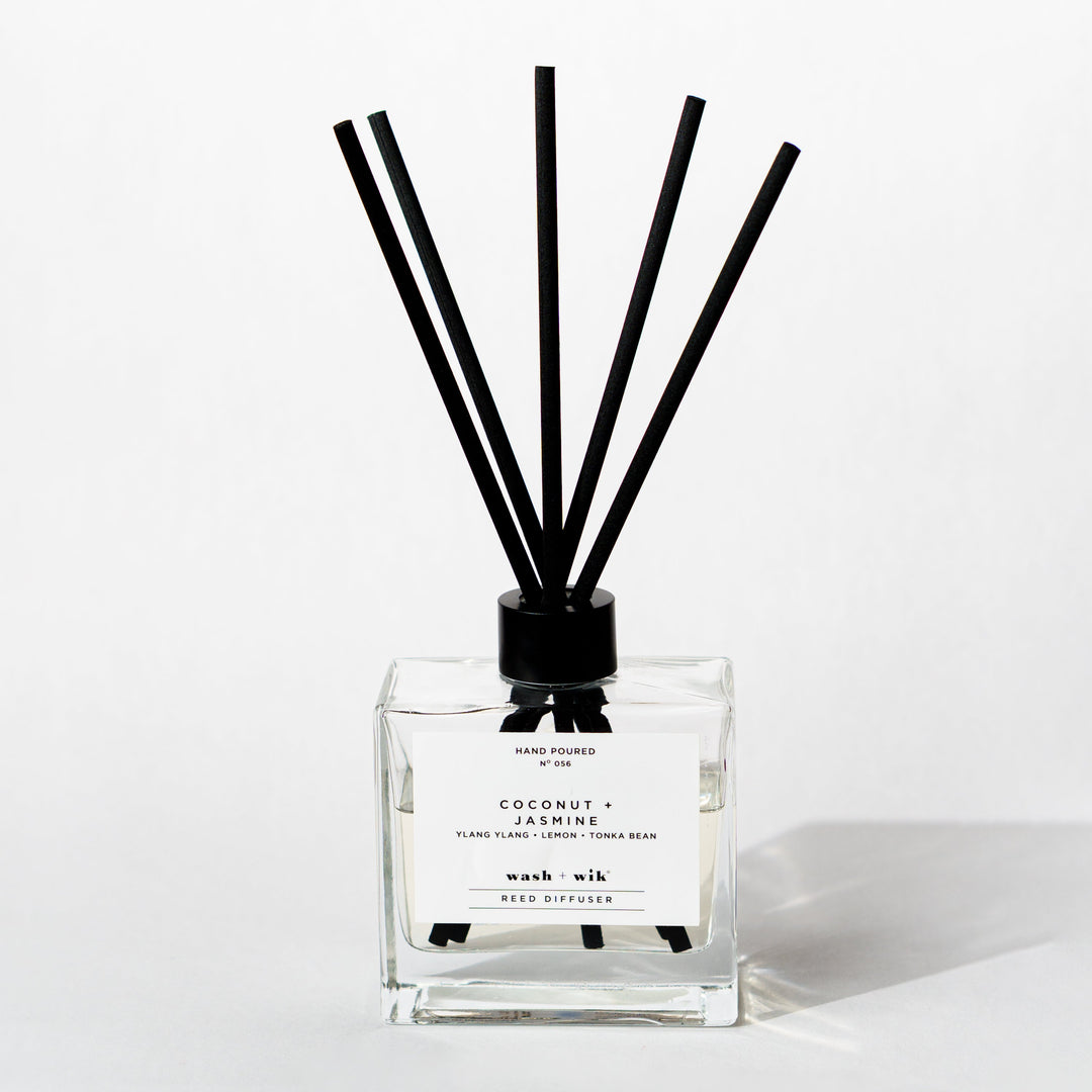 A clear glass reed diffuser bottle with a black cap and five black reeds
