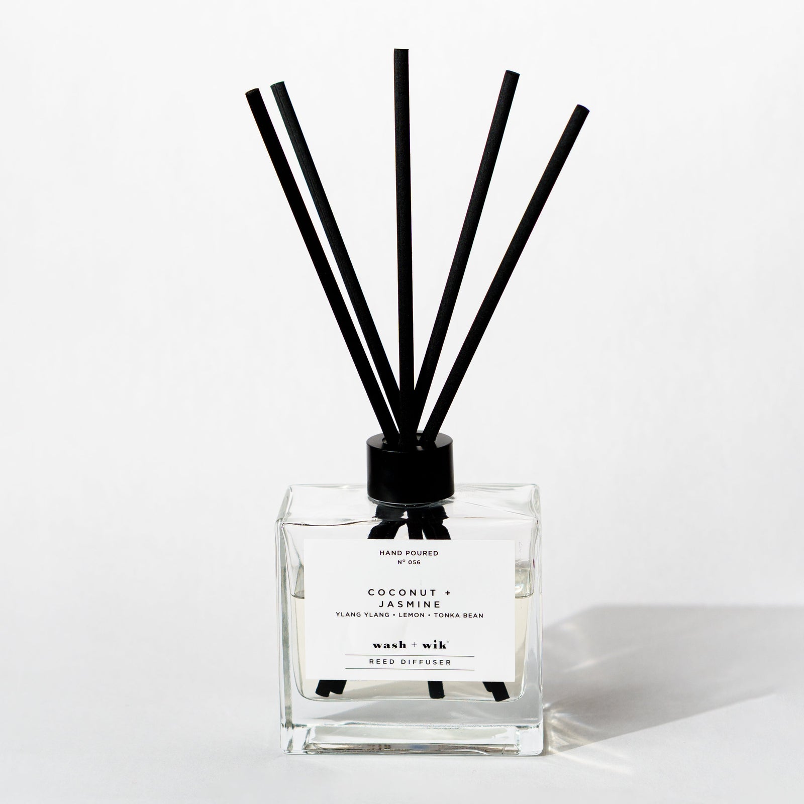 A clear glass reed diffuser bottle with a black cap and five black reeds