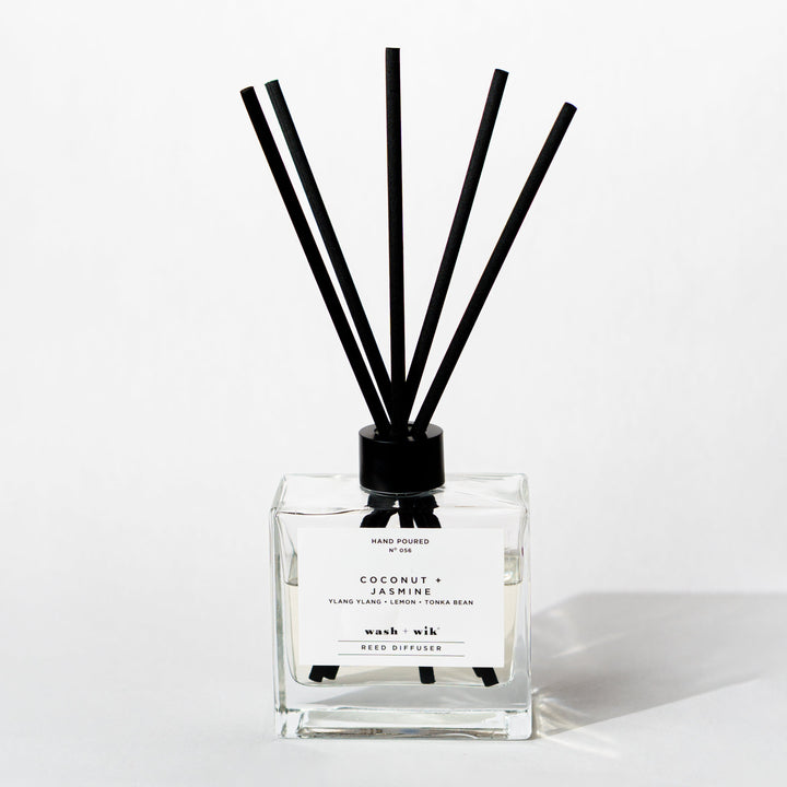 A clear glass reed diffuser bottle with a black cap and five black reeds